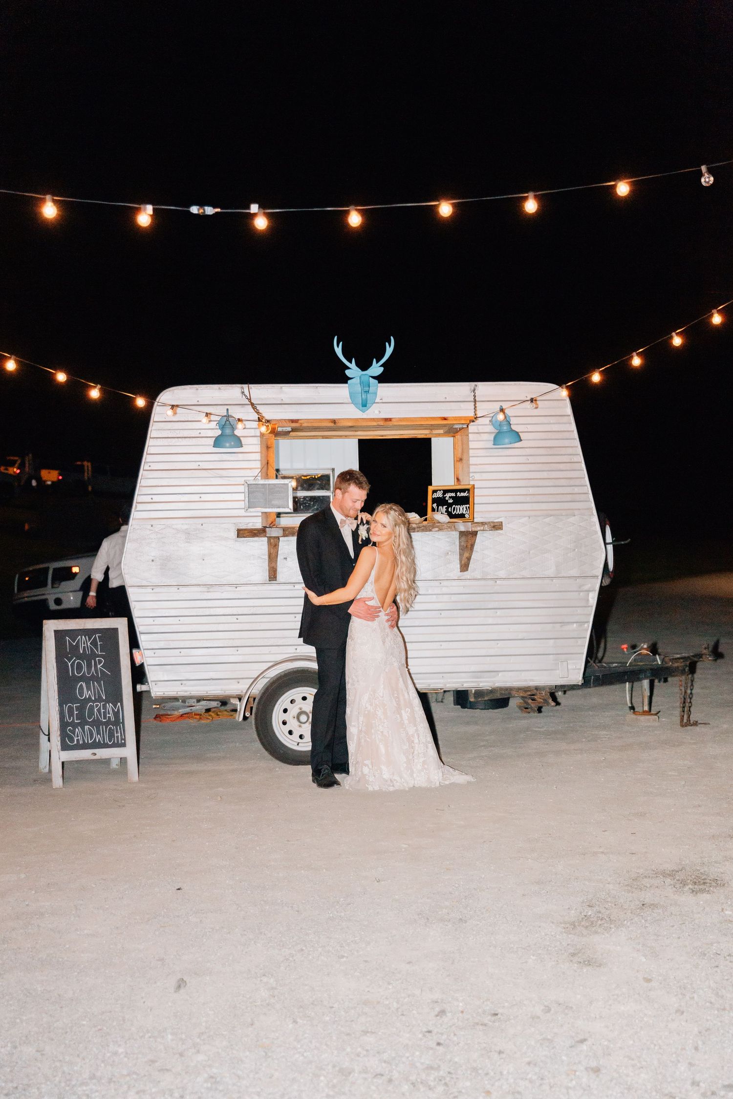 Wedding couple poses in front of illuminated retro camper trailer decorated with turquoise accents.