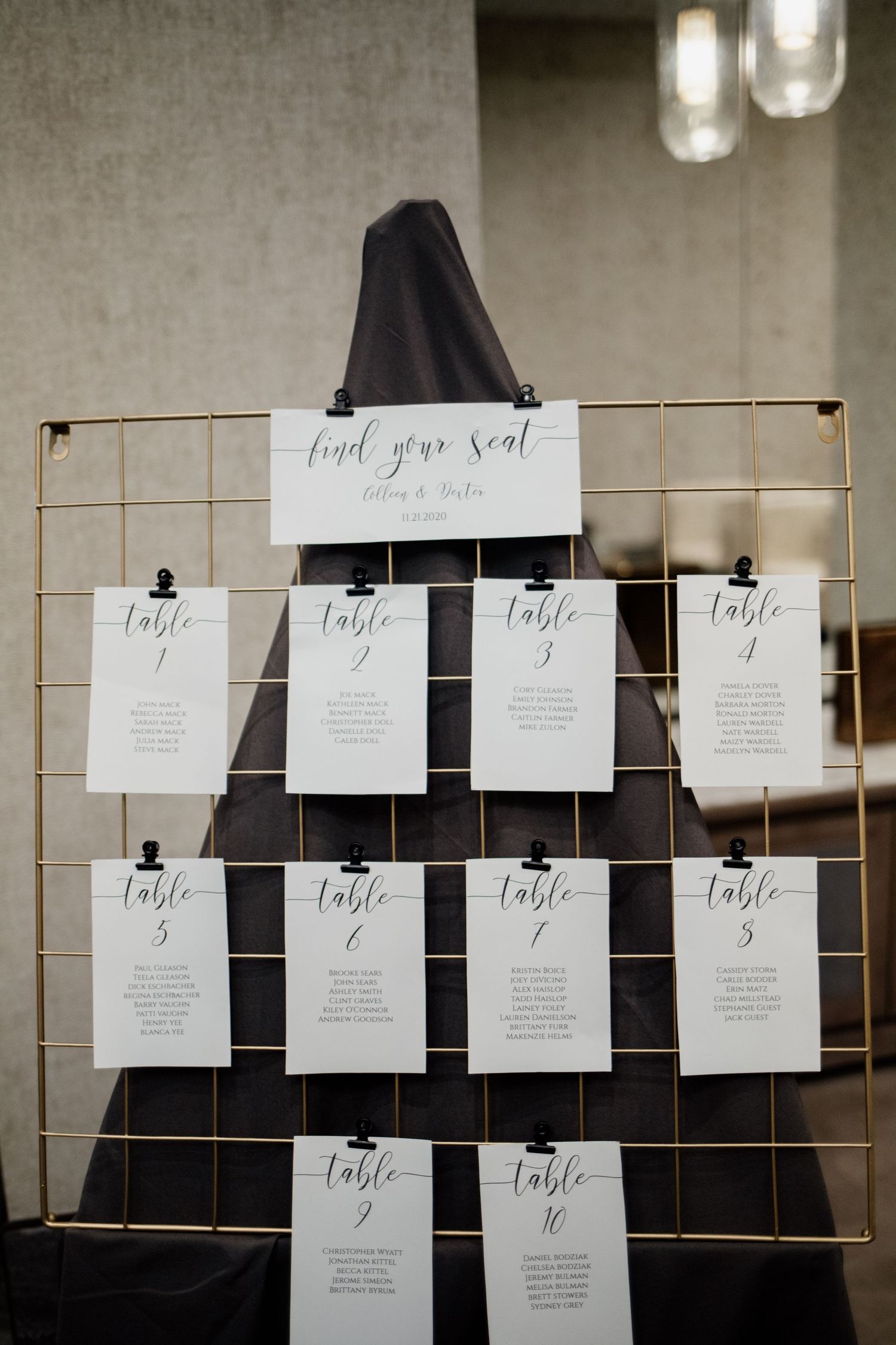 Wedding reception seating chart displayed on a gold wire grid with elegant black and white table cards.