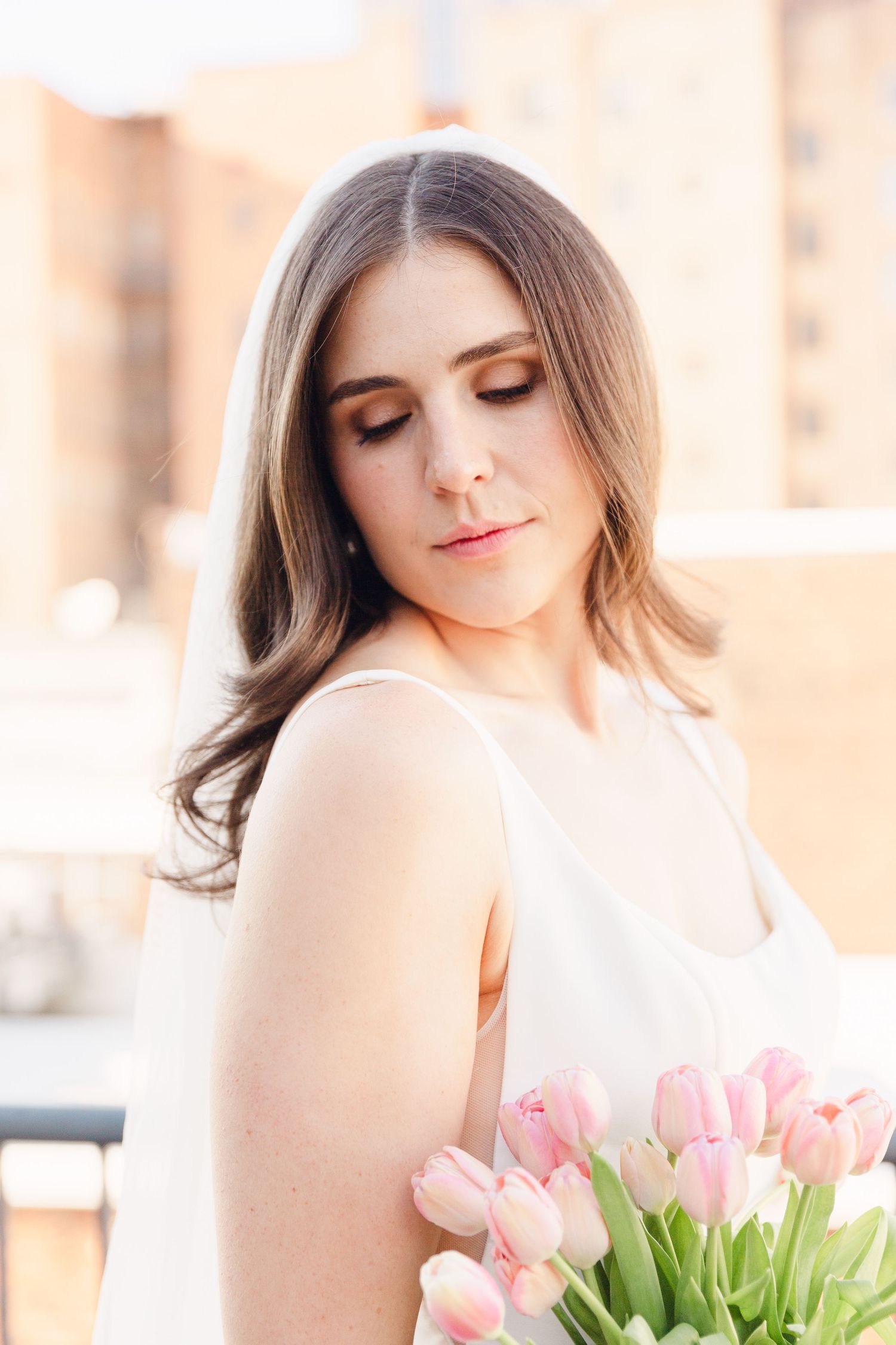 Elegant bridal portrait featuring soft makeup and pink tulips against an urban backdrop.