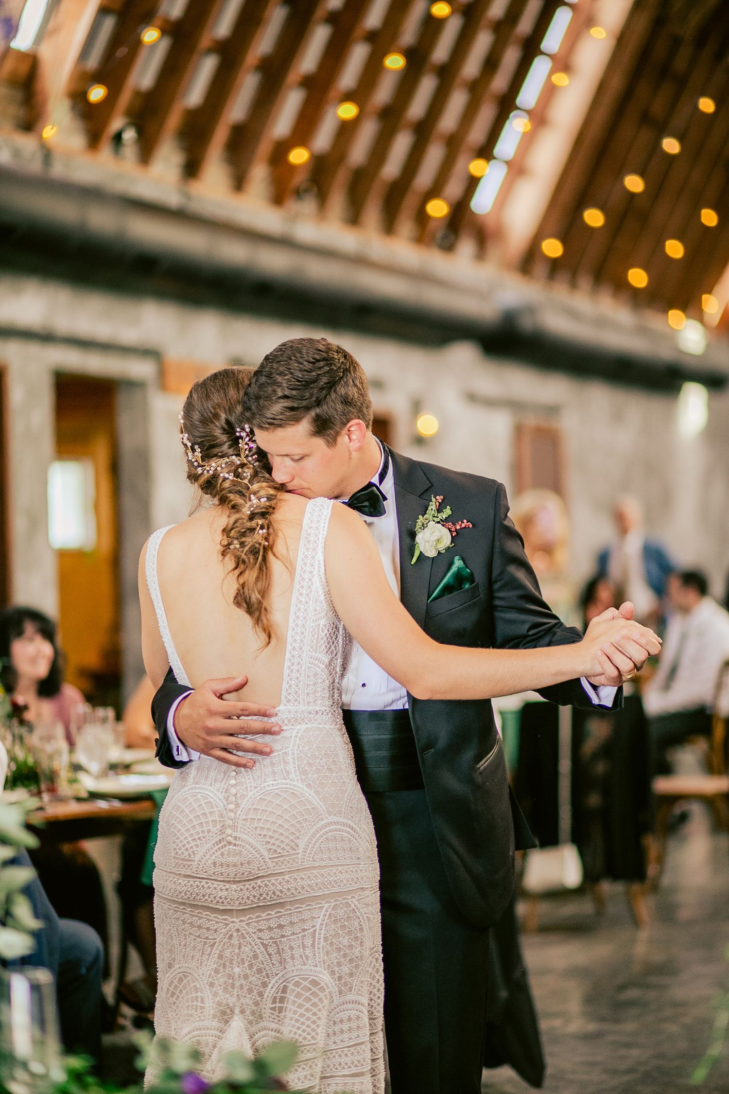 Couple dancing together at a wedding reception under warm string lights.