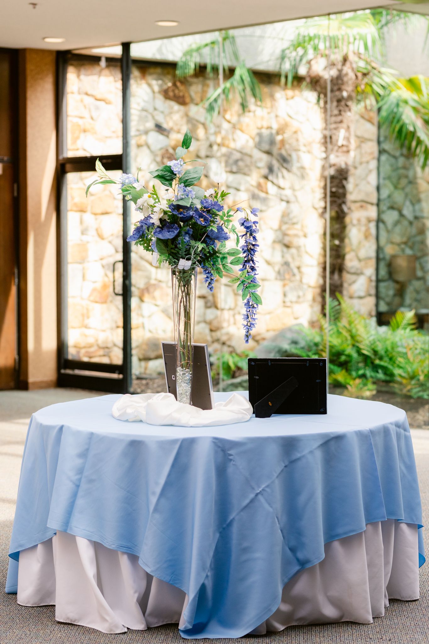 Round tables with light blue tablecloths and floral centerpieces arranged for an elegant outdoor event setting.