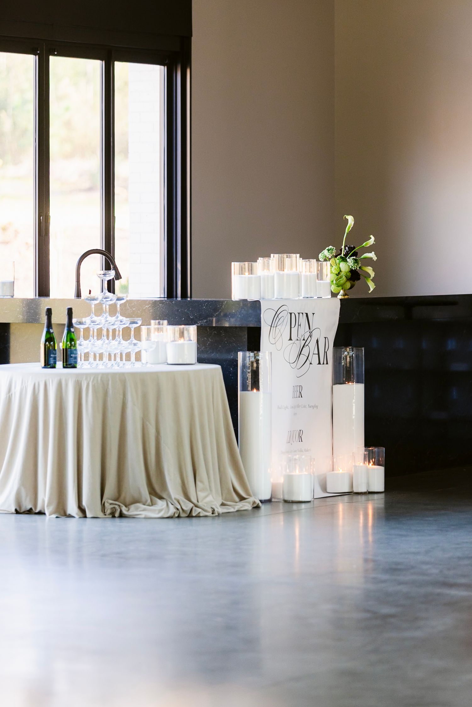 Modern event space with elegant white-draped tables and bar stations arranged along windows.