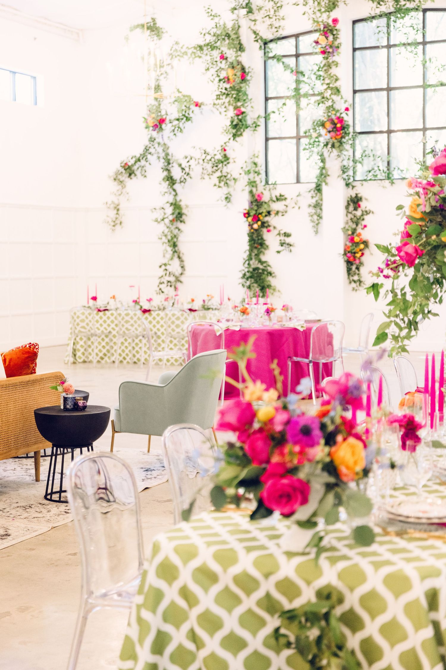 Modern wedding reception tables with pink floral centerpieces and geometric patterned linens in a bright venue.