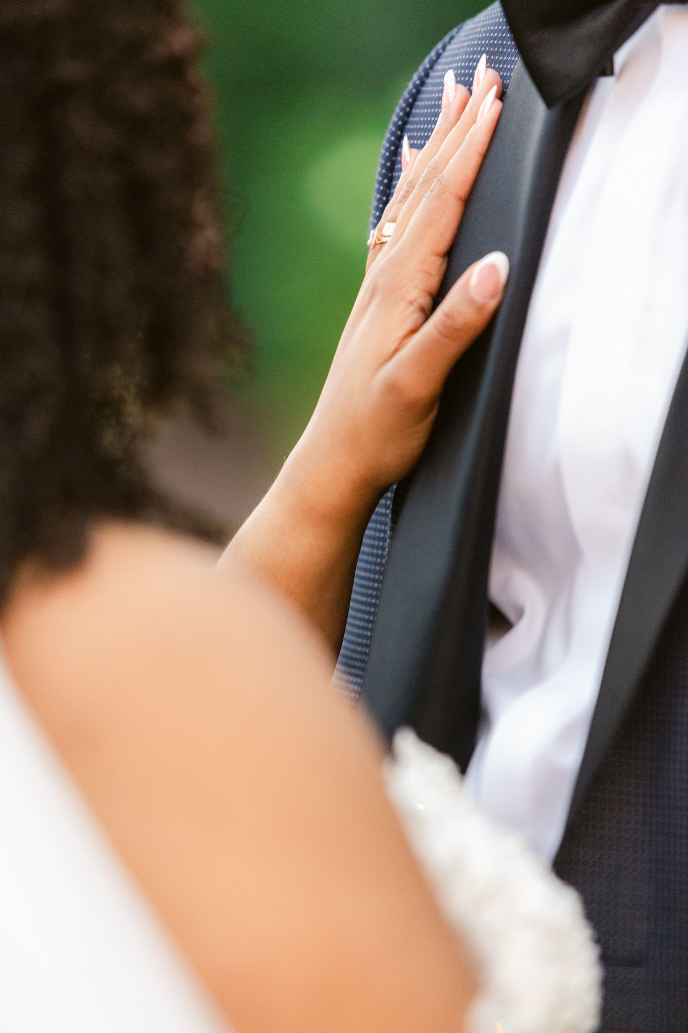 Close-up of hands adjusting a formal black suit jacket against a blurred green outdoor background.