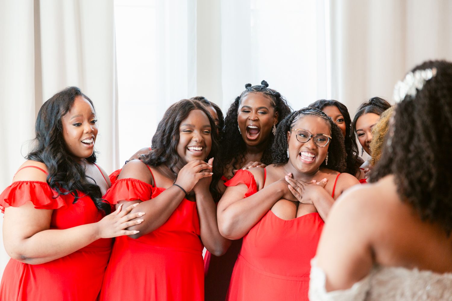 A group of women in red dresses laugh and embrace while standing together in a line.
