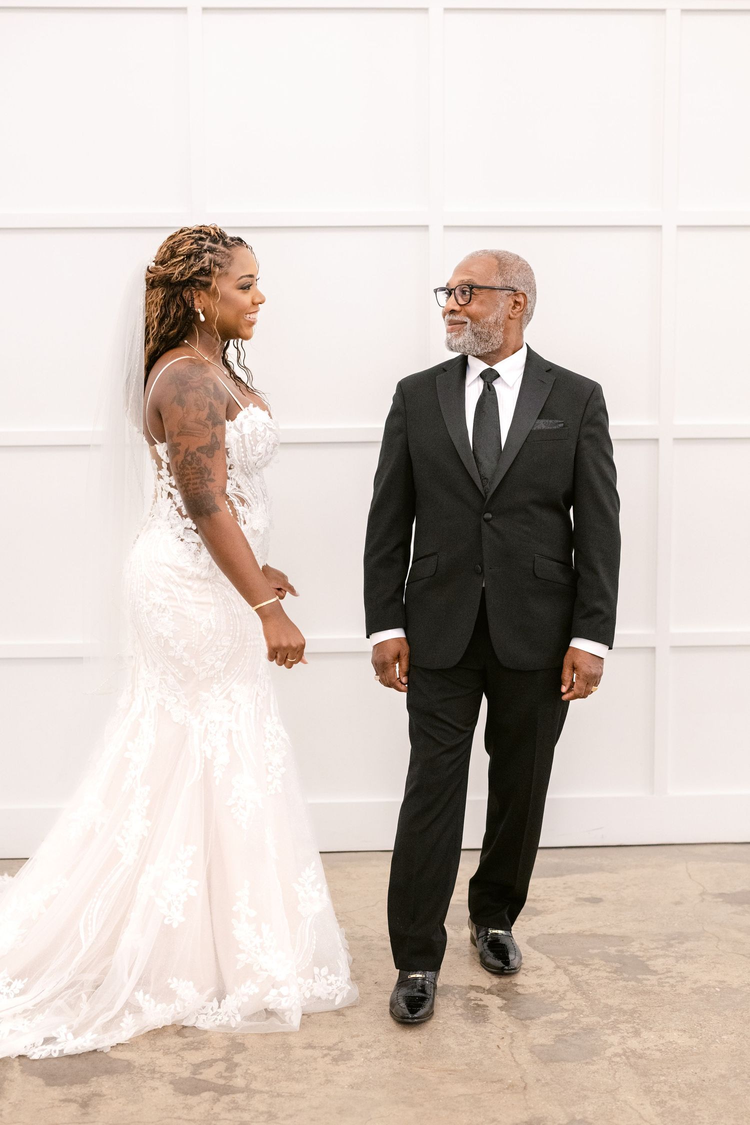A bride in a white lace gown shares a sweet moment with someone in a black suit before the ceremony.