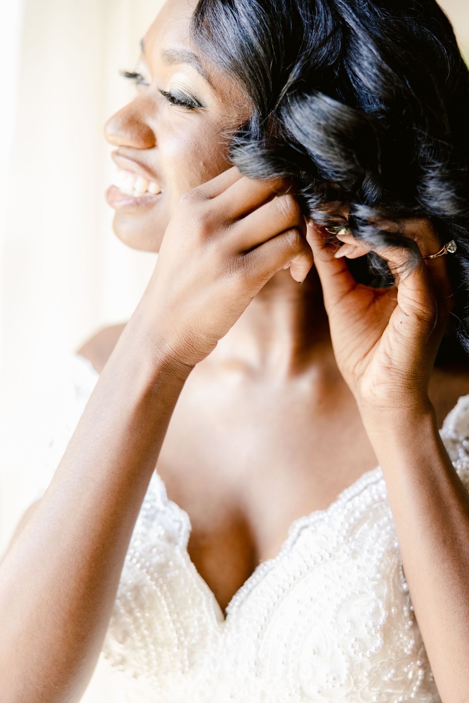 A close-up profile shot shows someone in a white lace dress putting on an earring while smiling.