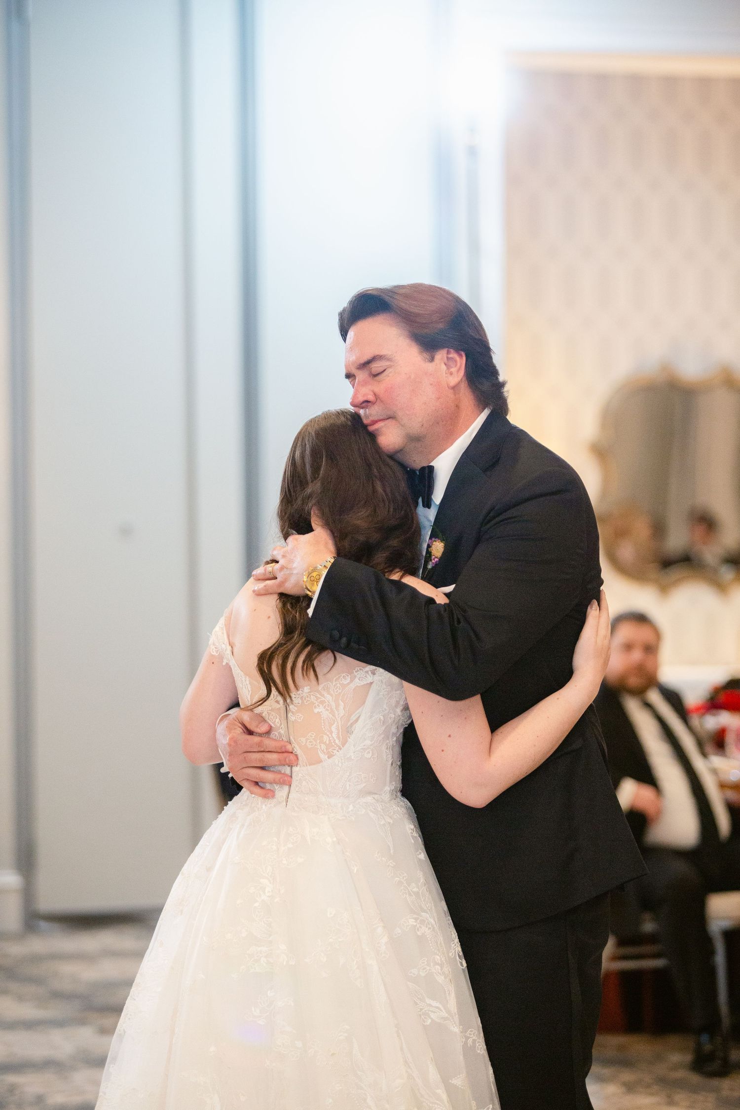 A couple shares an intimate dance moment in a well-lit ballroom during a wedding celebration.