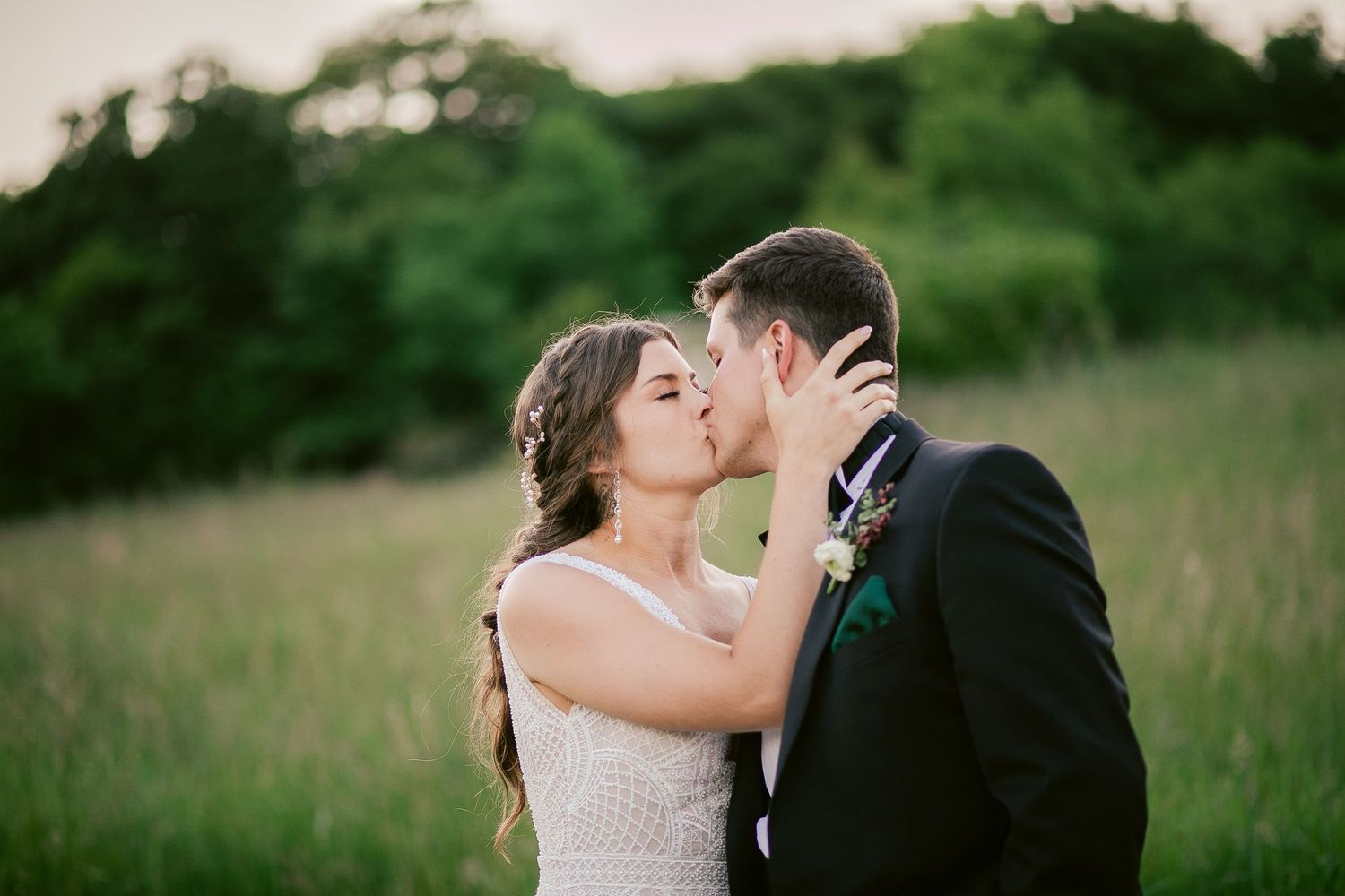 Intimate wedding portrait captured in tall grass during golden hour.
