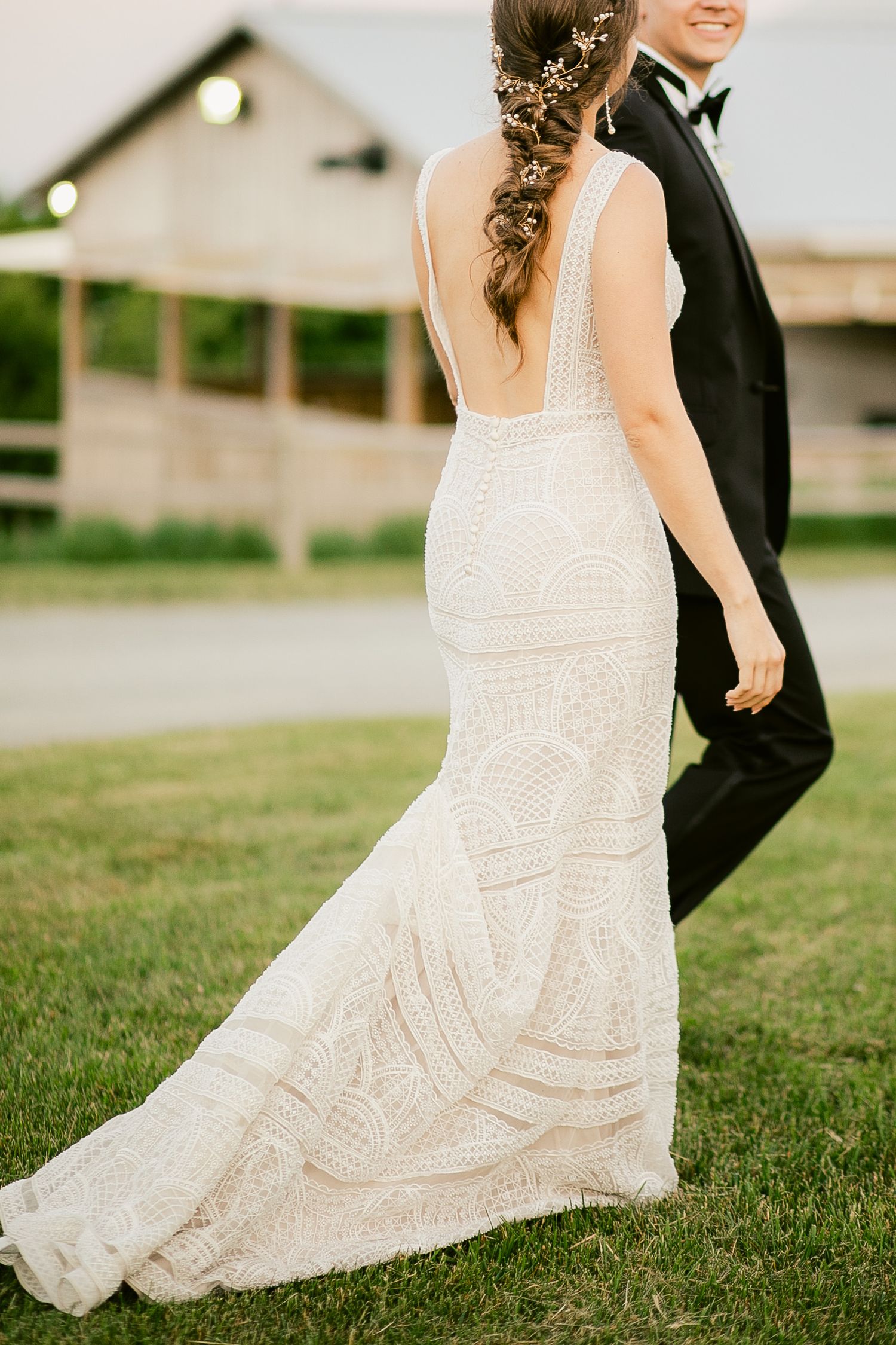 A flowing lace wedding dress train trails across green grass during an outdoor photo session.