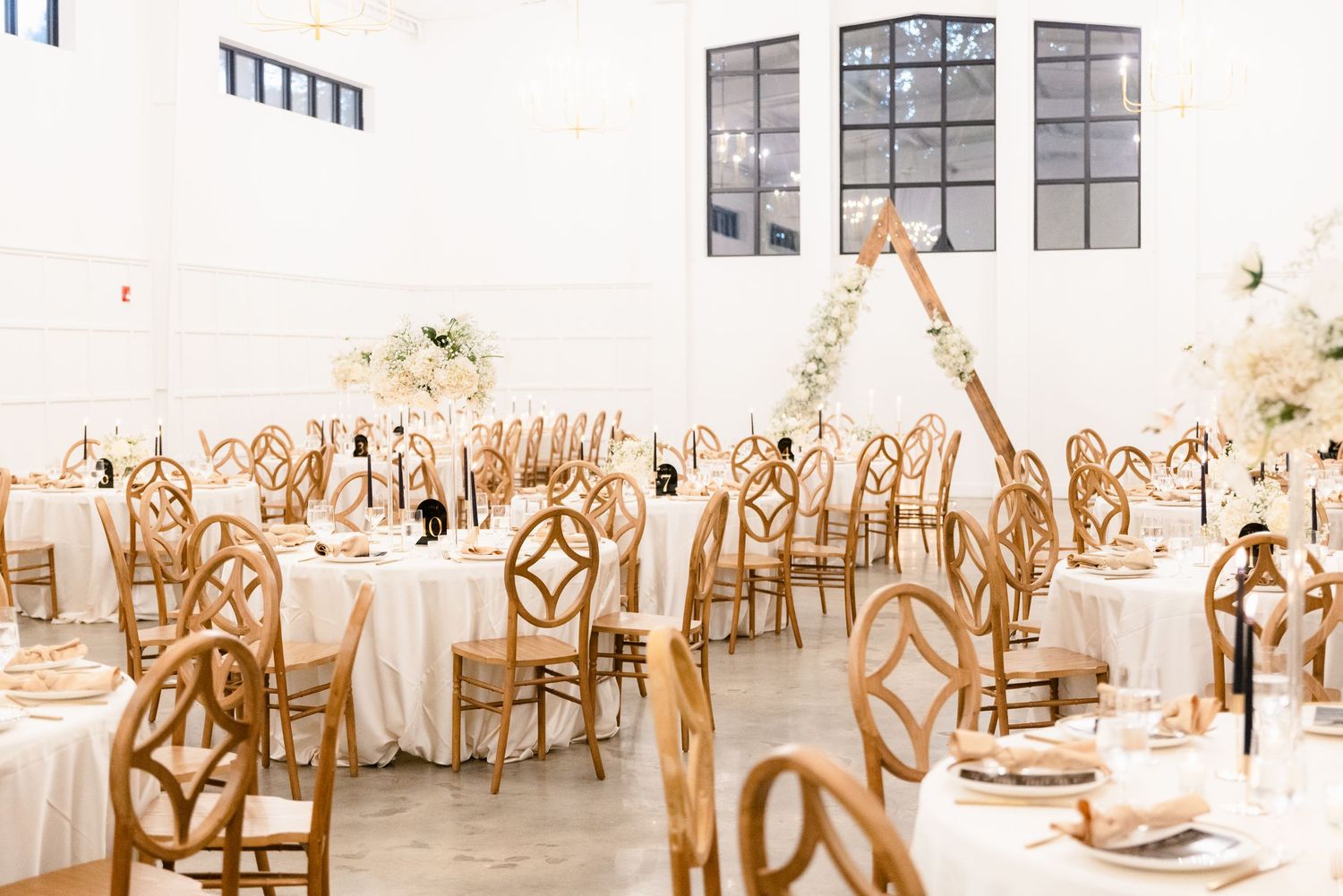 Wedding reception tables decorated in white and gold with elegant place settings and floral centerpieces in a bright venue.