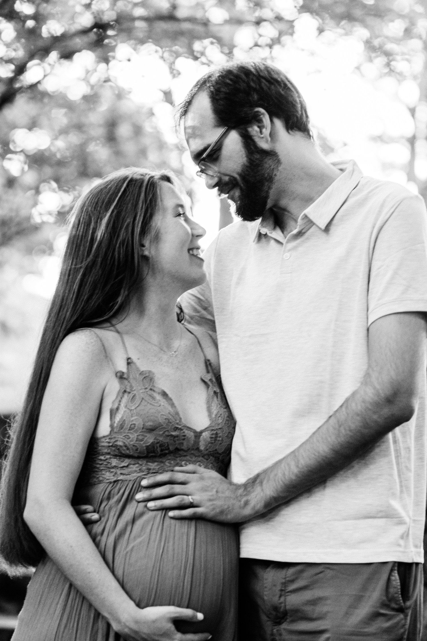 Expecting couple sharing intimate moment outdoors in black and white.