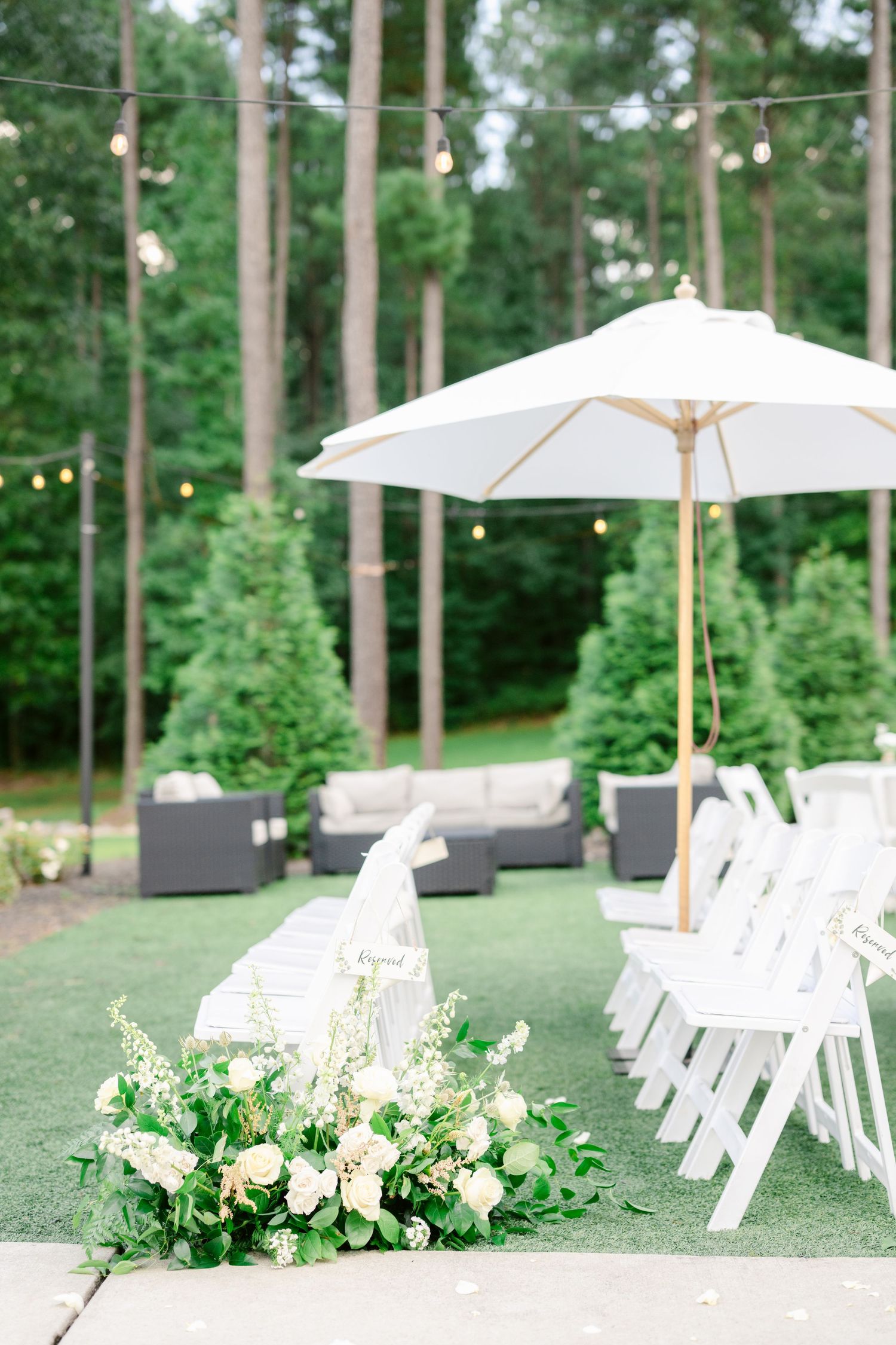 White chairs and umbrellas set up for an elegant outdoor wedding ceremony in a serene pine forest setting.