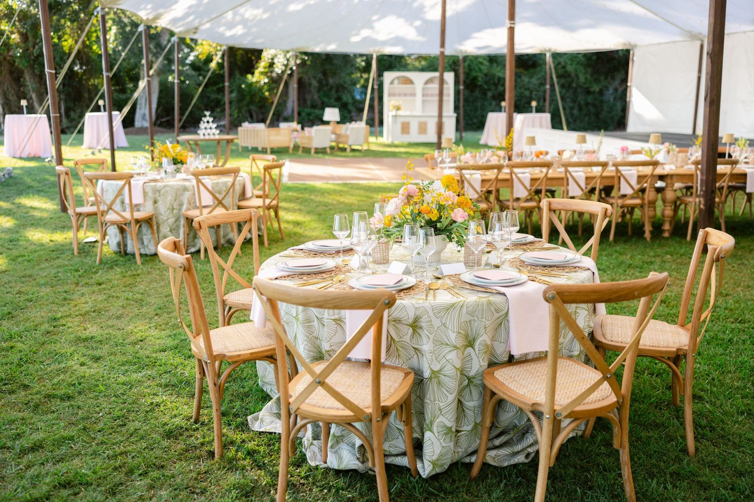 Outdoor wedding reception setup with wooden chairs and floral centerpieces under a white tent.