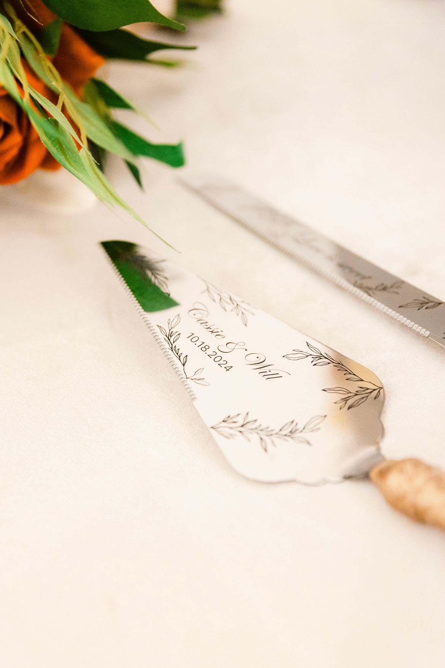 Elegant wedding cake server with delicate floral design and orange roses in soft focus background.