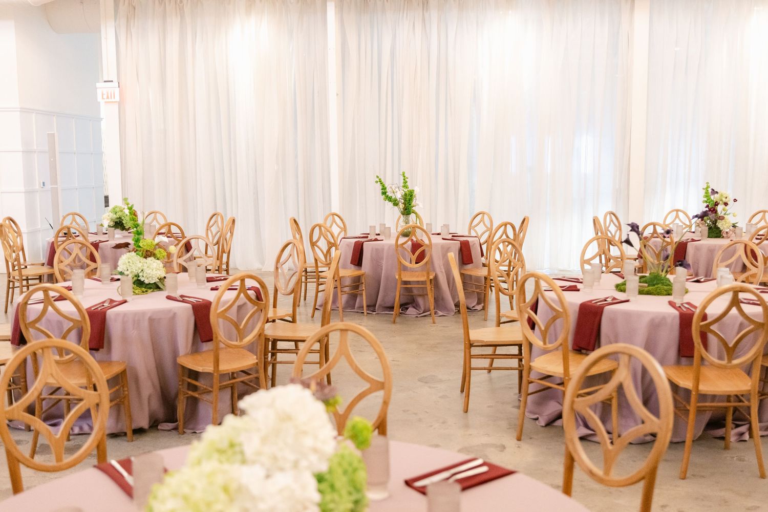 Elegant wedding reception venue with wooden chairs and white drapes creating a romantic, ethereal atmosphere.
