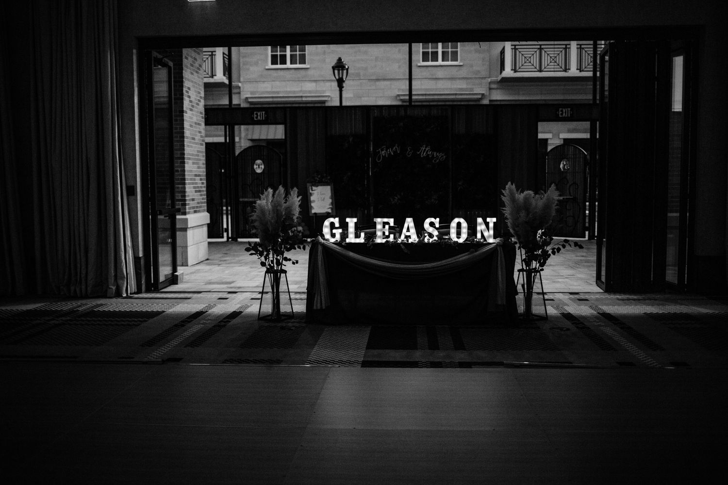 Black and white photo of illuminated 'Gleason' signage on storefront exterior.