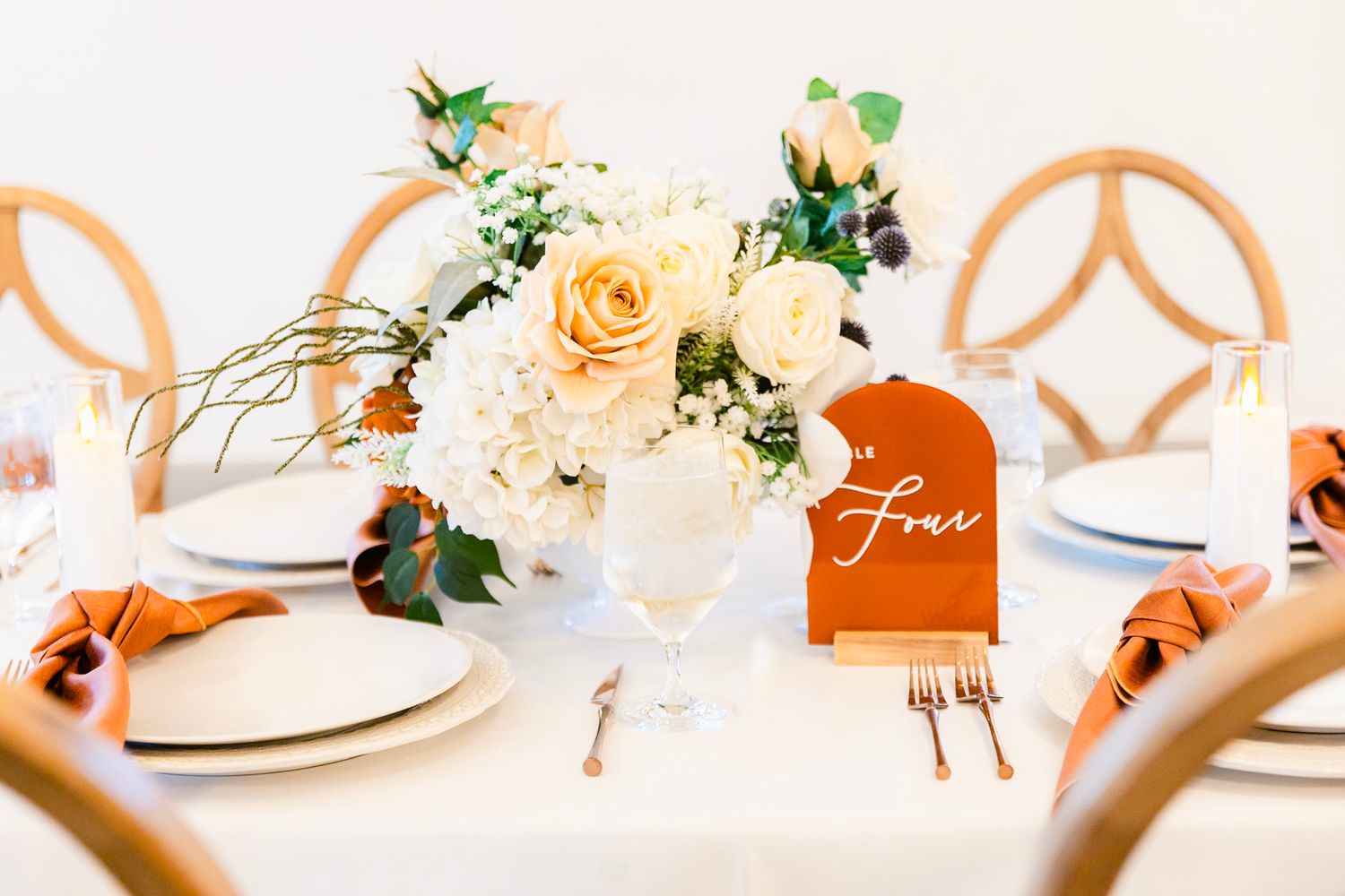 Close up of wedding table decor with peach roses centerpiece and orange place card against white dinnerware.