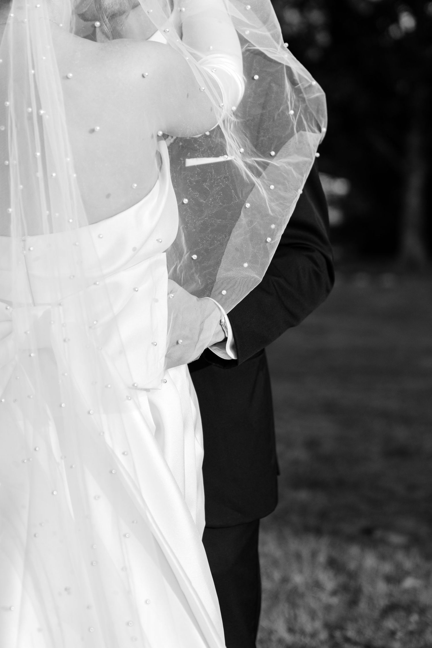 Black and white wedding photo showing a close embrace between bride in white dress and groom in dark suit.