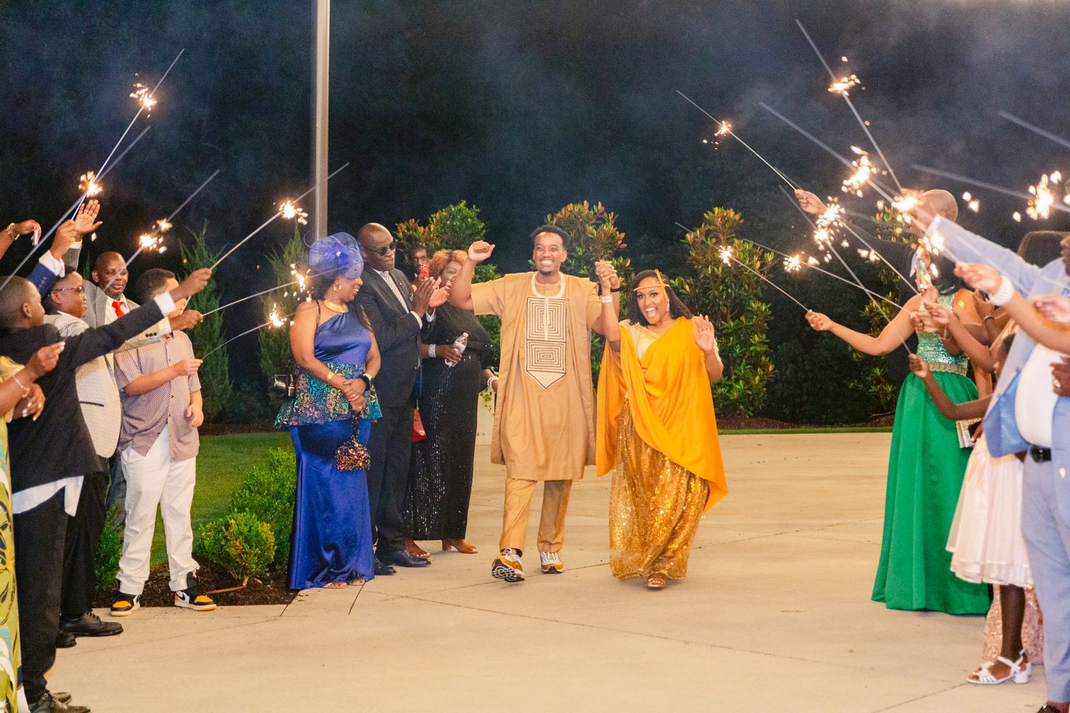 Wedding guests hold sparklers creating a magical nighttime tunnel for celebration at an outdoor reception.