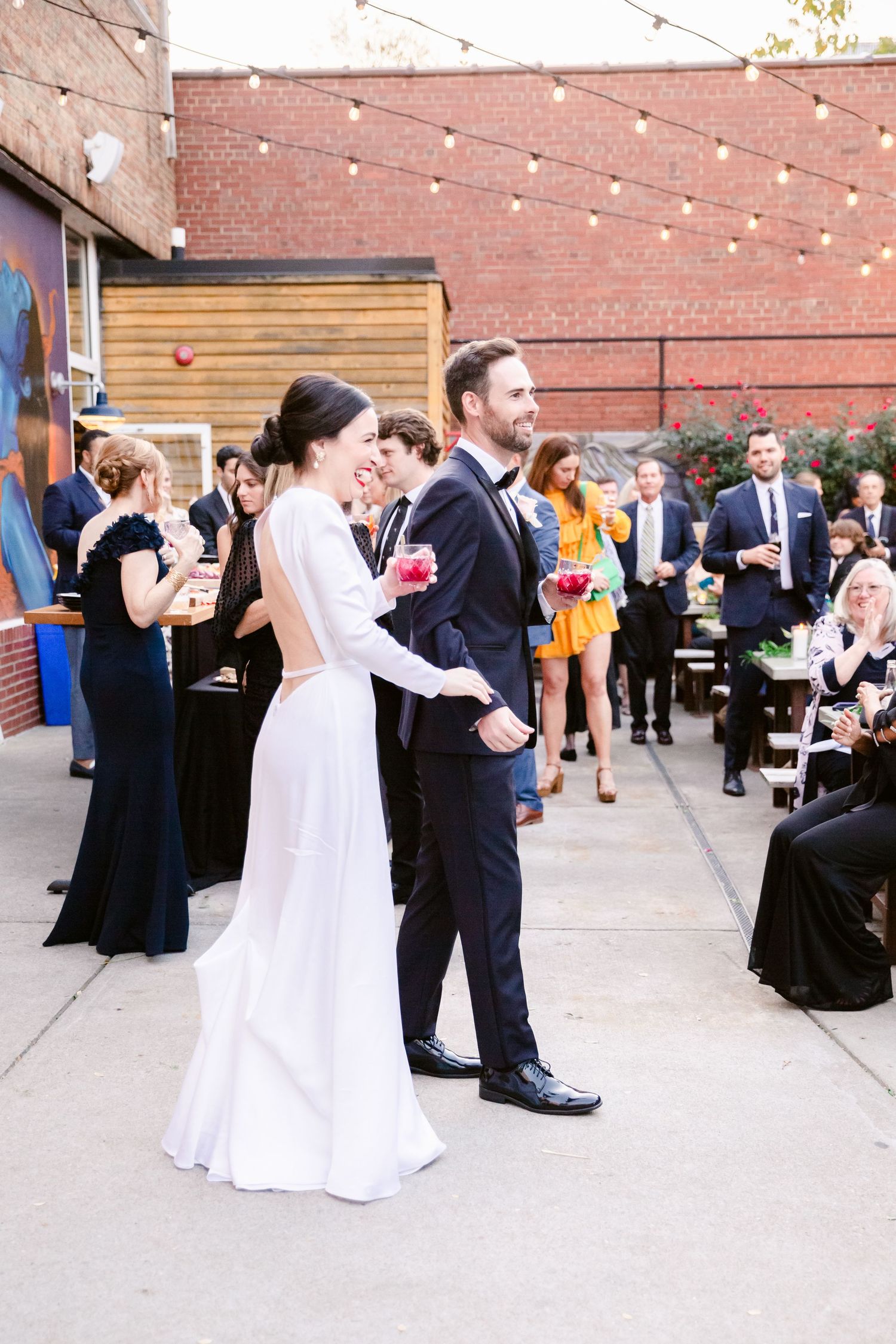 Newlyweds celebrate during their reception on an outdoor patio decorated with string lights.