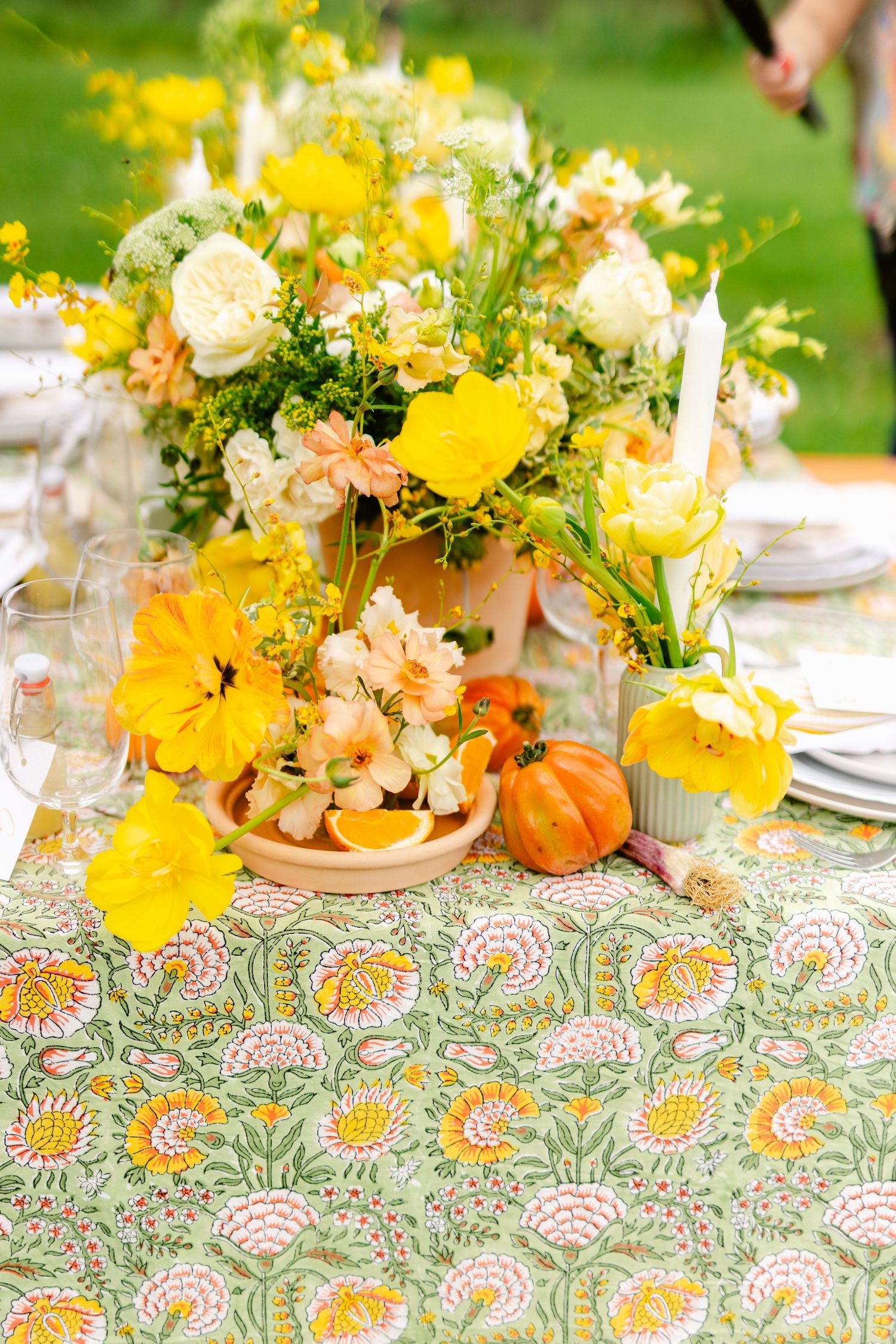 Vibrant fall table setting with yellow flowers, small pumpkins and paisley tablecloth creating an elegant autumn display.