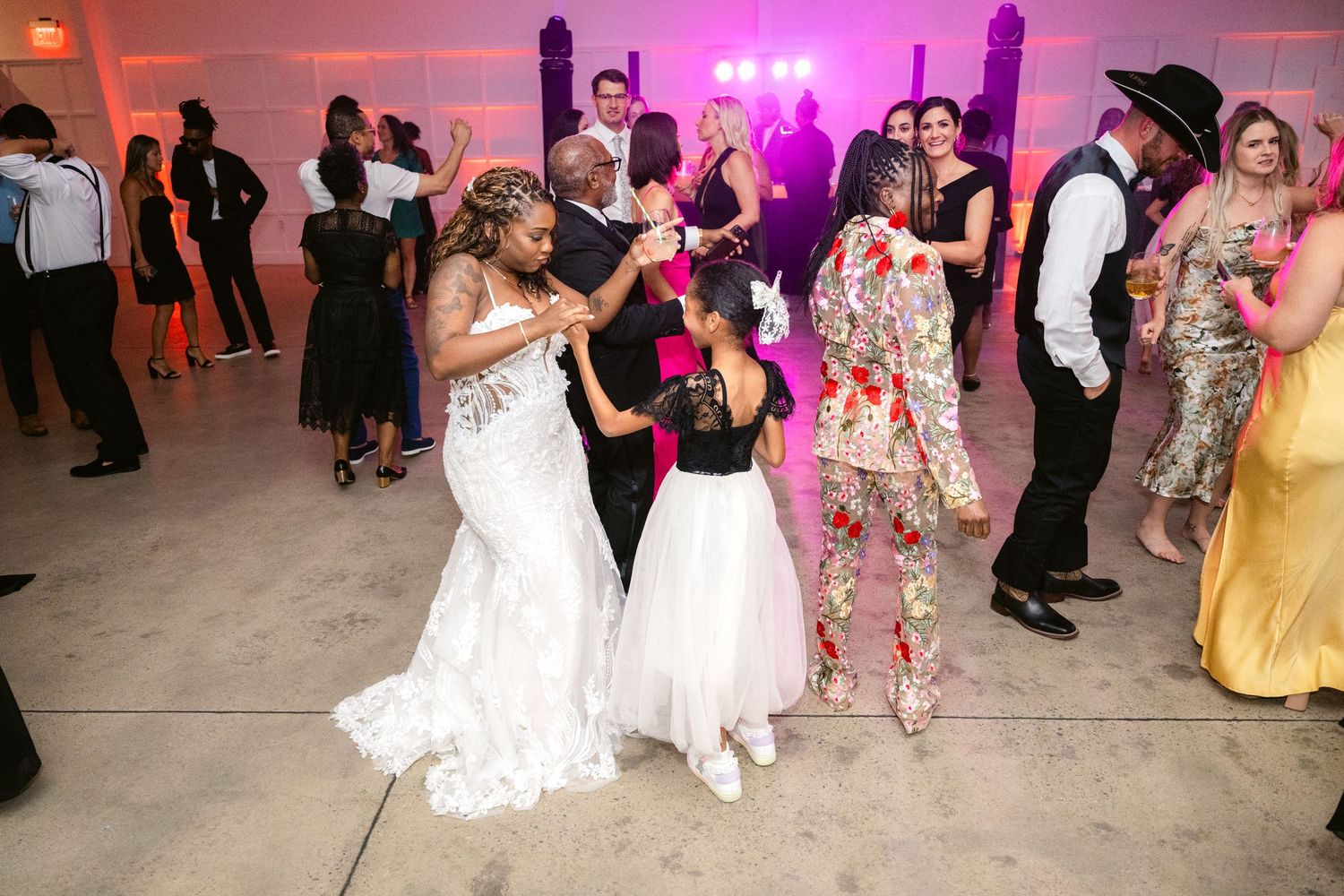 Wedding guests dancing on a dance floor illuminated by pink and purple lighting at an evening reception.