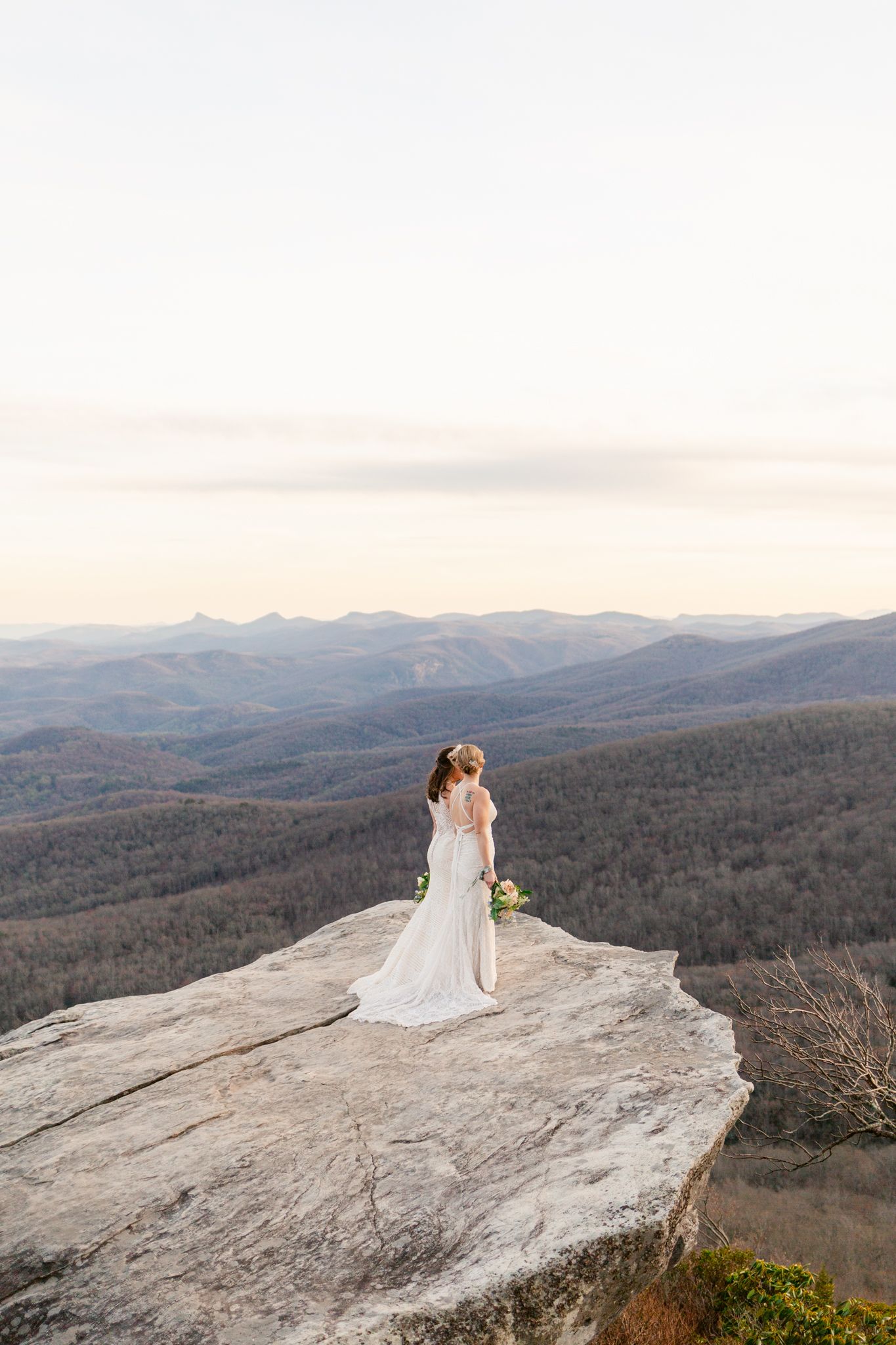 A couple shares a romantic moment on a scenic mountain overlook with sweeping views of rolling hills at sunset.