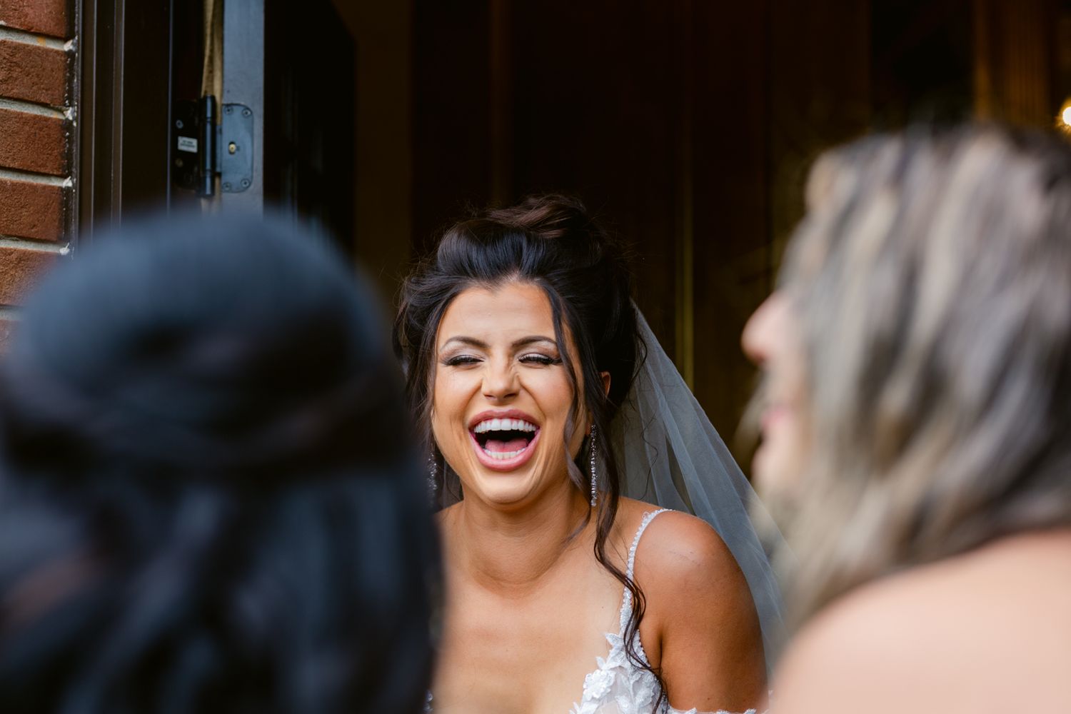 A bride in a white wedding dress laughs joyfully during a candid moment with wedding guests.