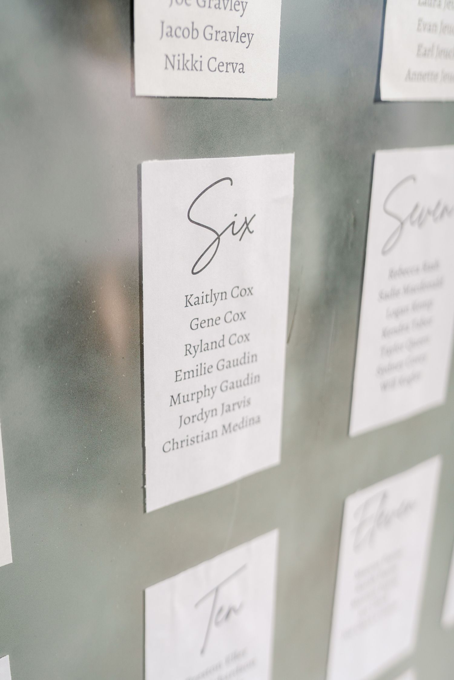Wedding seating chart with guest names printed on white paper cards arranged on a wall.