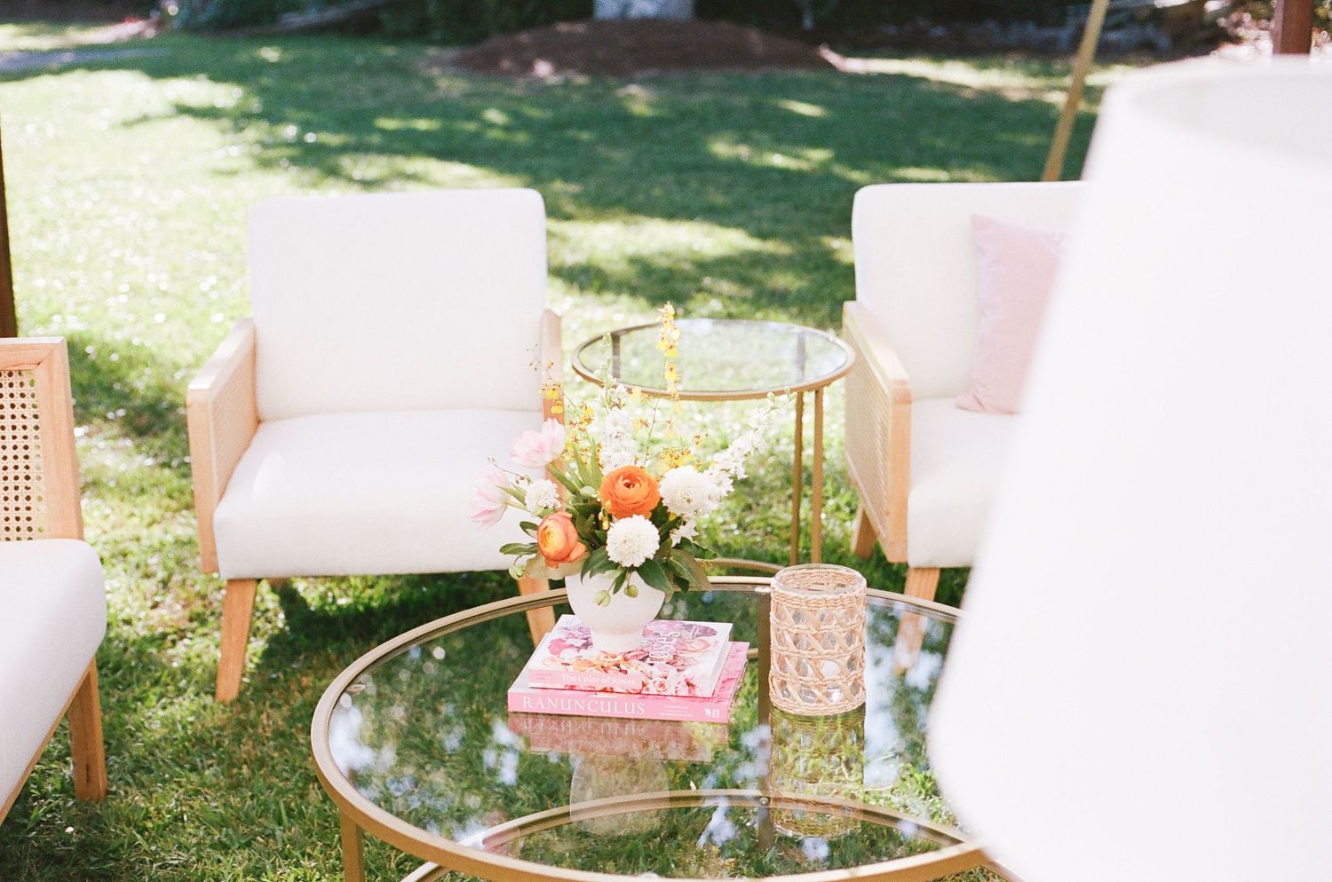 Elegant outdoor lounge area with white chairs and pink accents for a garden wedding.
