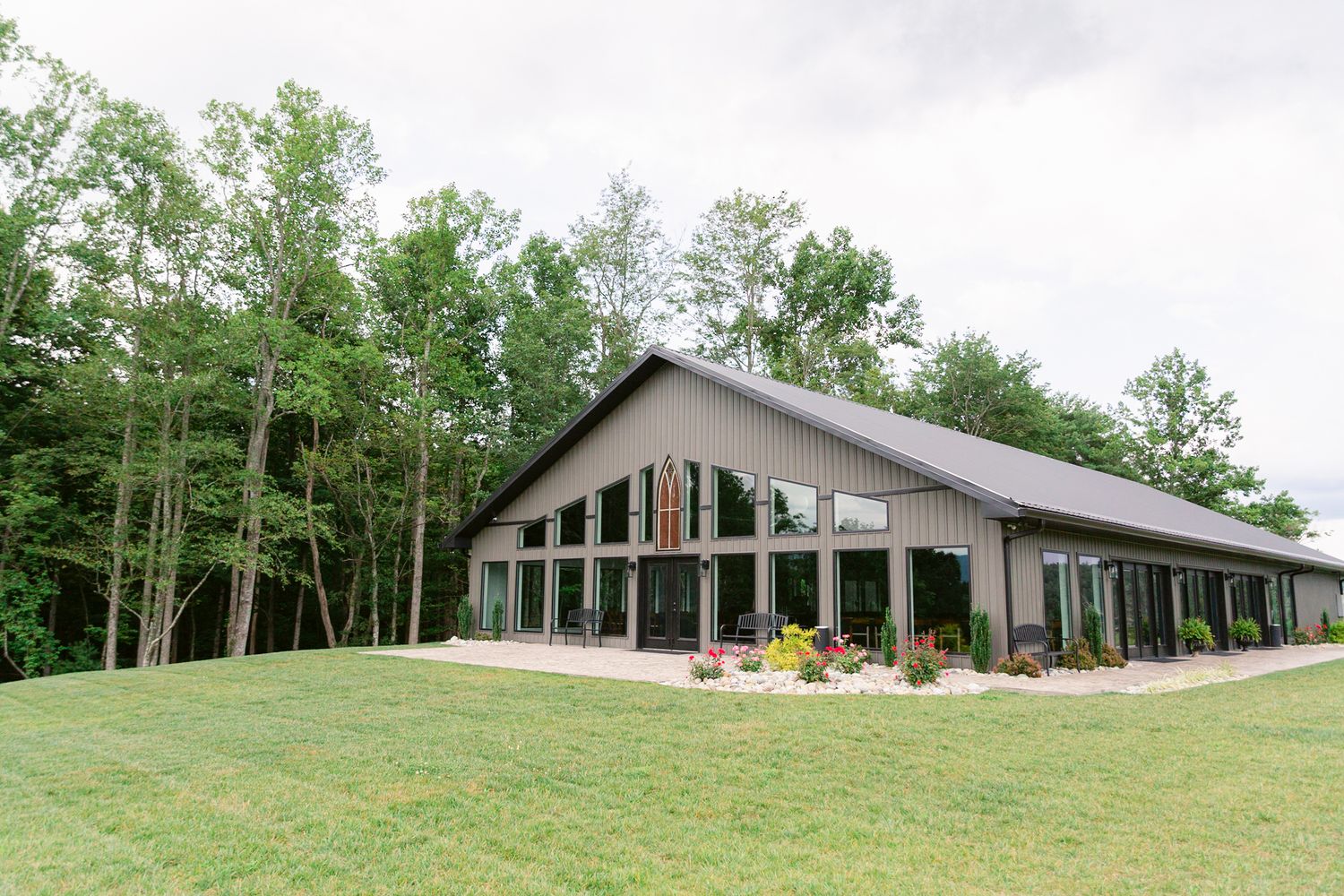 A panoramic view of a rustic barn-style building nestled among green trees on a grassy hillside.