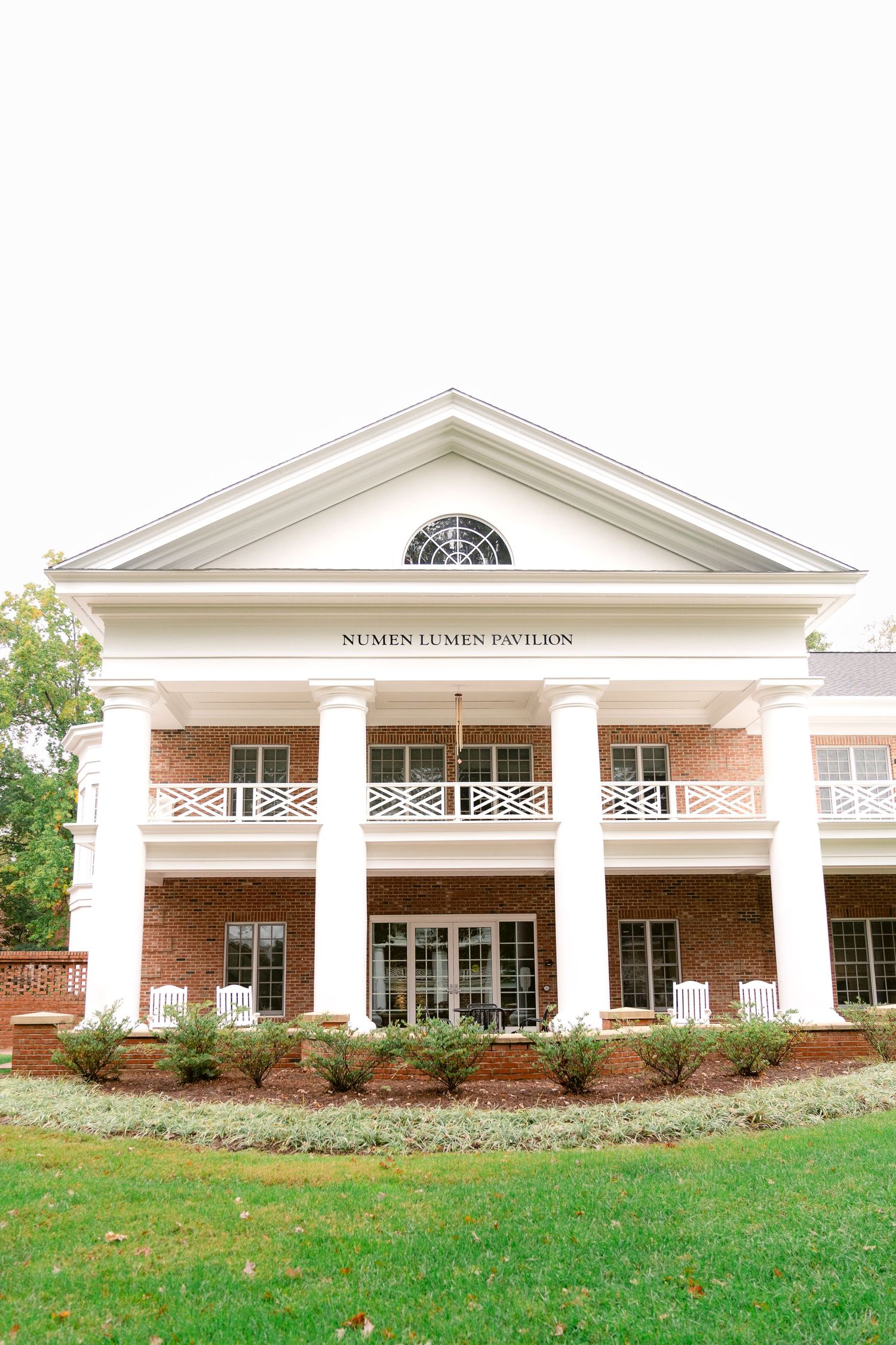 Elegant white-columned Numen Lumen pavilion building with brick facade and classical architectural details.