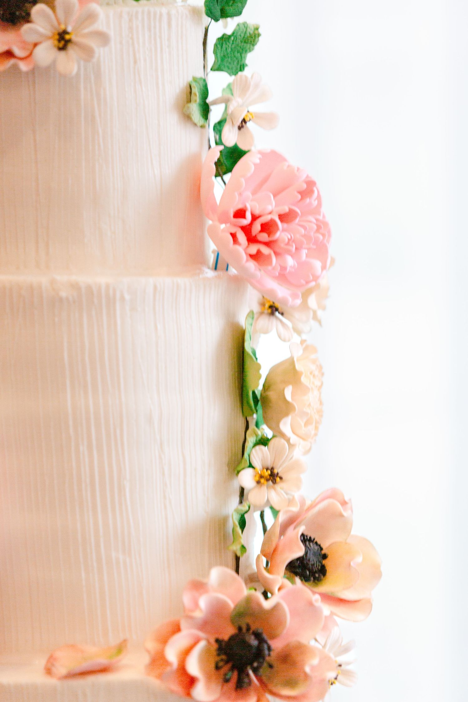Delicate sugar flowers in peach and coral tones cascade down the side of a white tiered wedding cake.