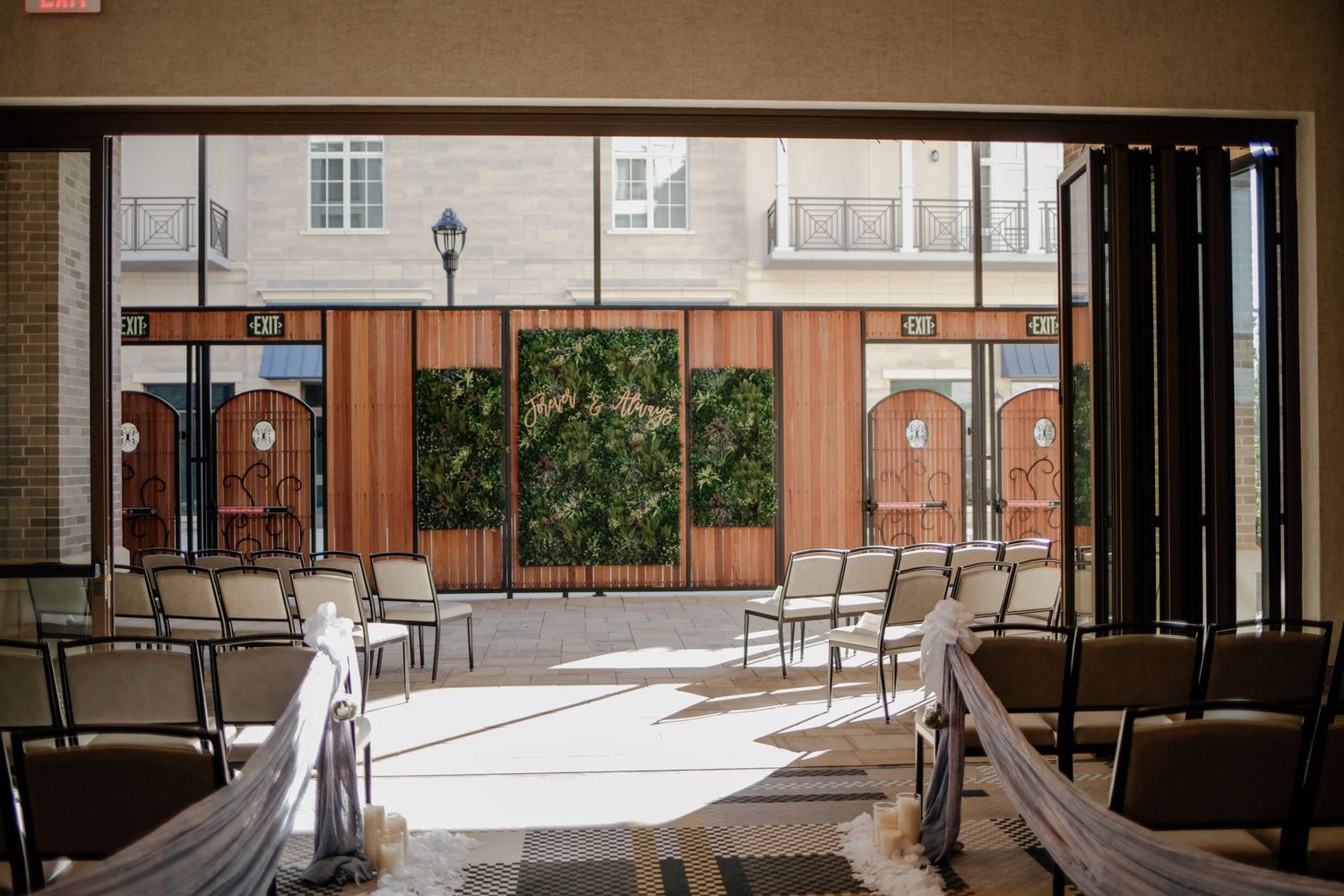 Empty wedding ceremony space with white chairs and greenery wall backdrop.