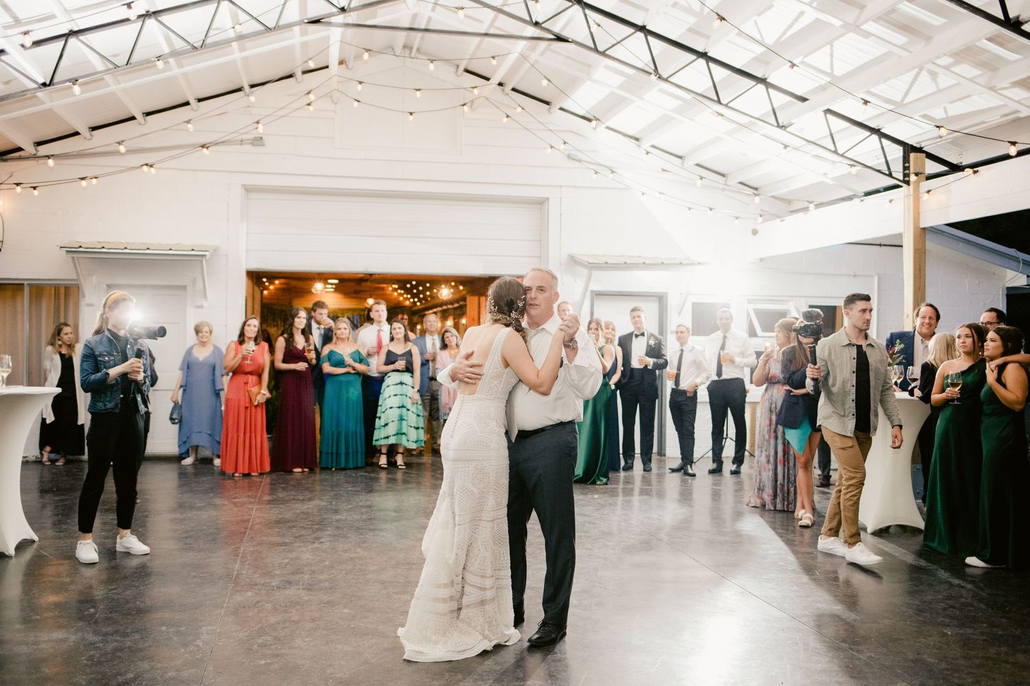 A couple shares their first dance surrounded by guests in an industrial-style reception venue.