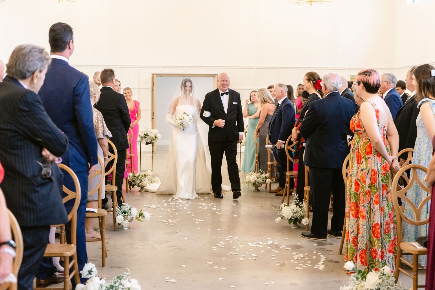 Wedding ceremony taking place in a bright indoor venue with guests seated in rows and an officiant at the altar.