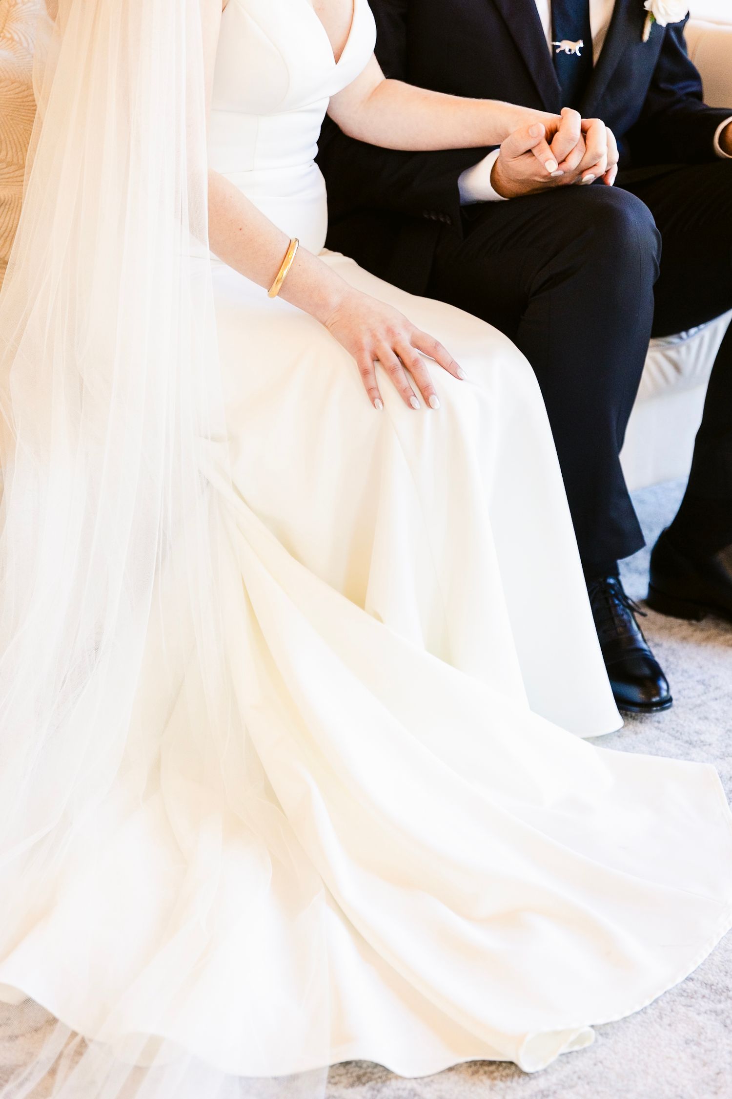 An elegant white wedding gown flows across a floor as a couple sits together during the ceremony.
