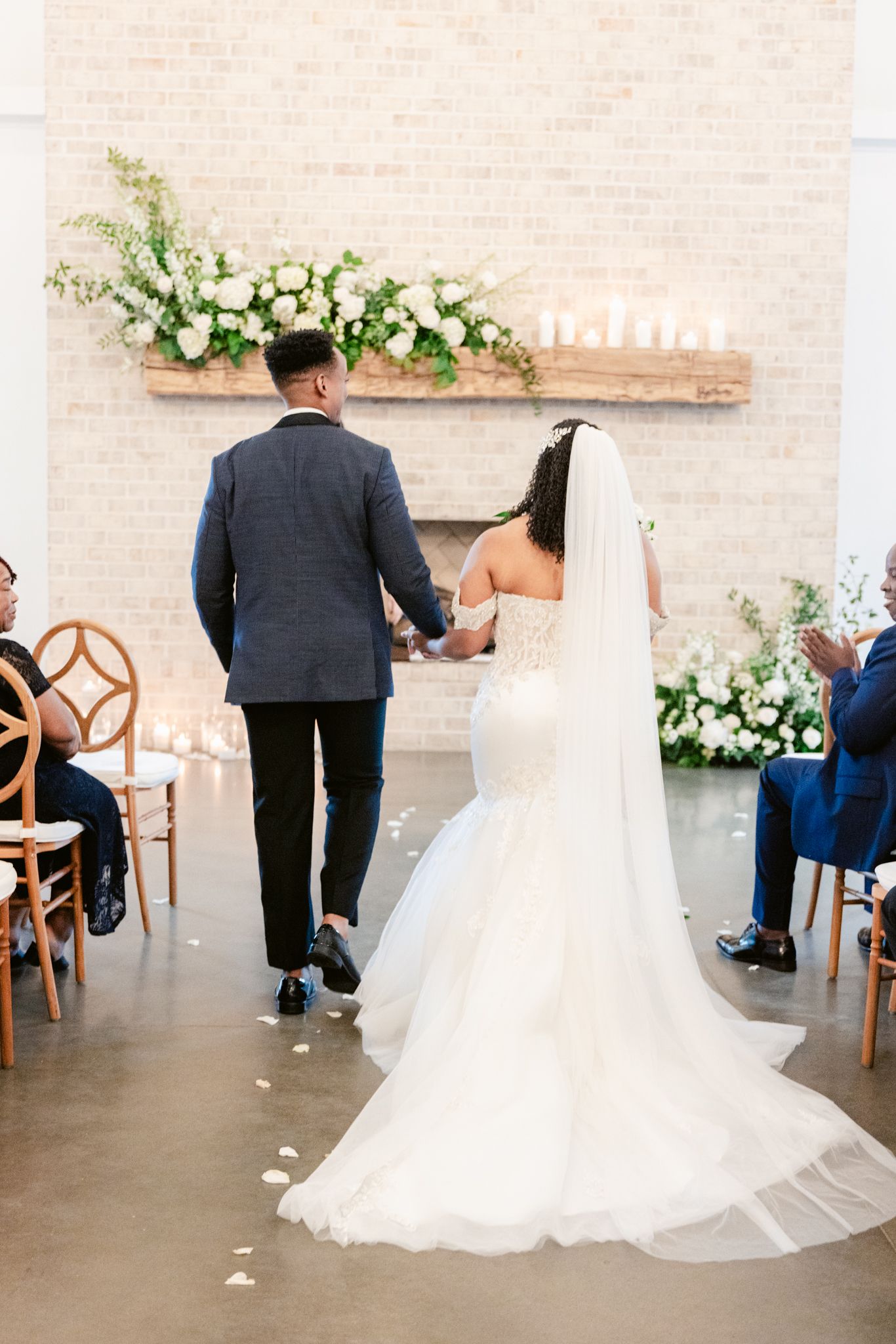 Elegant couple walks down aisle under floral arrangements and candlelight in modern wedding venue.