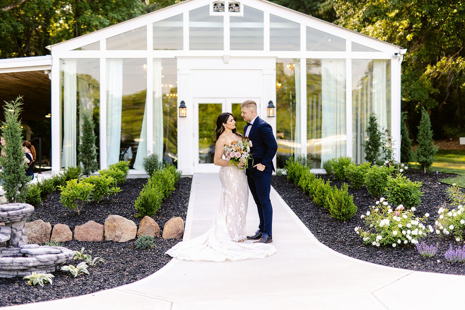 White greenhouse wedding venue with glass panels and landscaped gardens in golden sunlight.