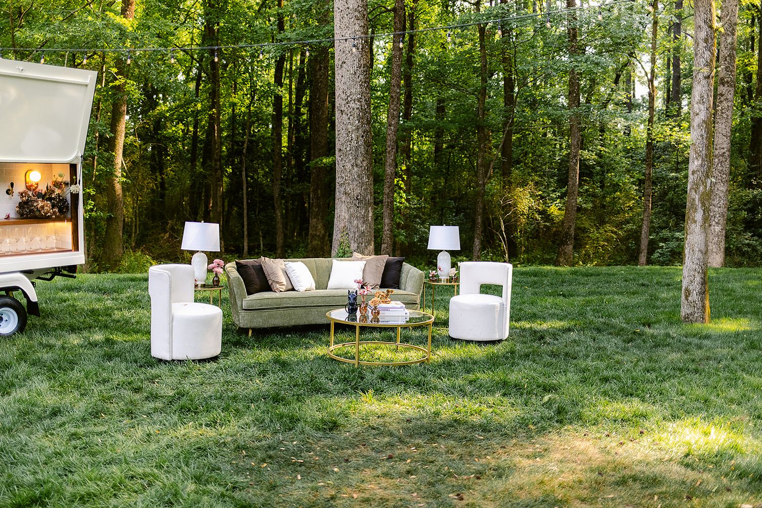 Outdoor wedding ceremony setup in a forest with white chairs and wooden arch decorated with flowers and greenery.