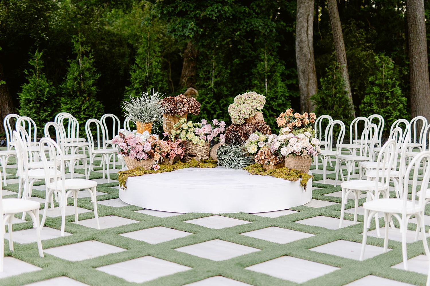White chairs arranged in rows for an outdoor garden wedding ceremony with floral decorations and greenery.