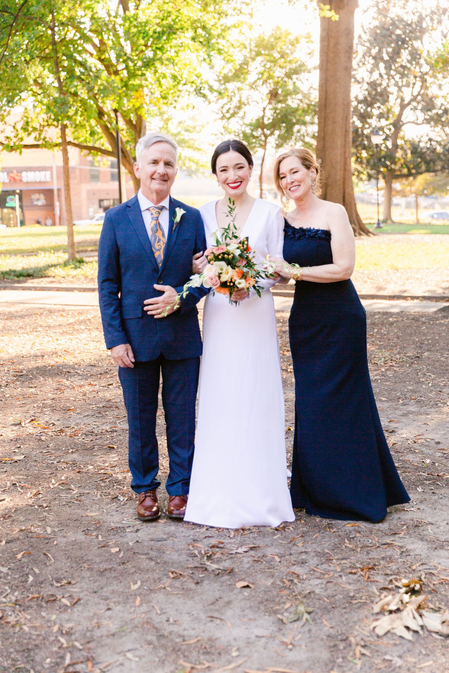Wedding party poses outdoors with bride in white gown and guests in navy blue formal attire.