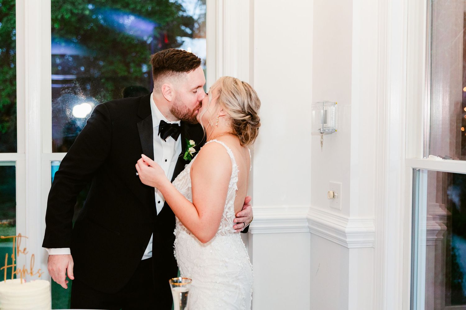 A romantic wedding couple shares a kiss near white columns during their elegant evening celebration.