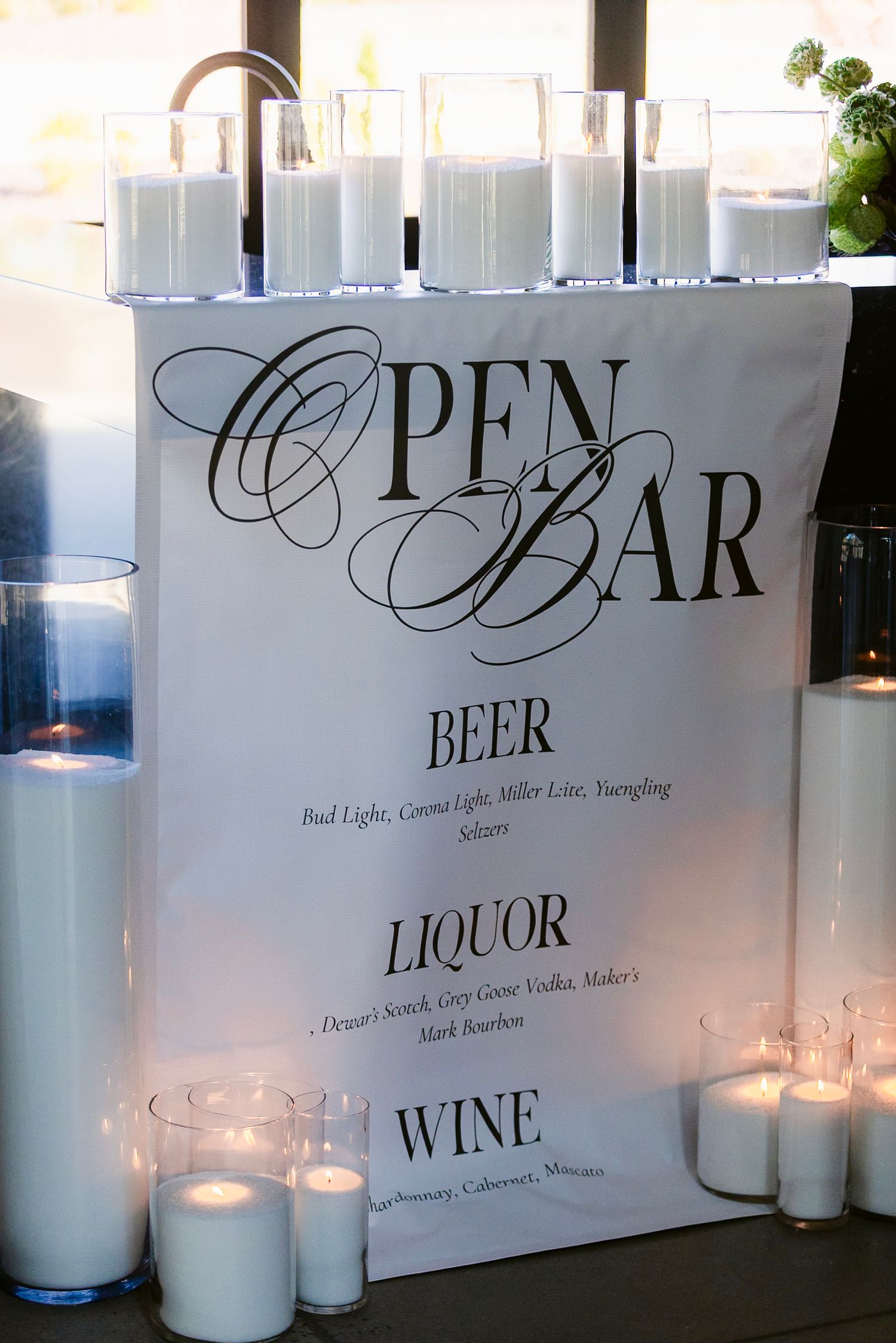 Elegant bar signage with 'Open Beer Liquor Wine' text illuminated by white candles in a sophisticated setting.