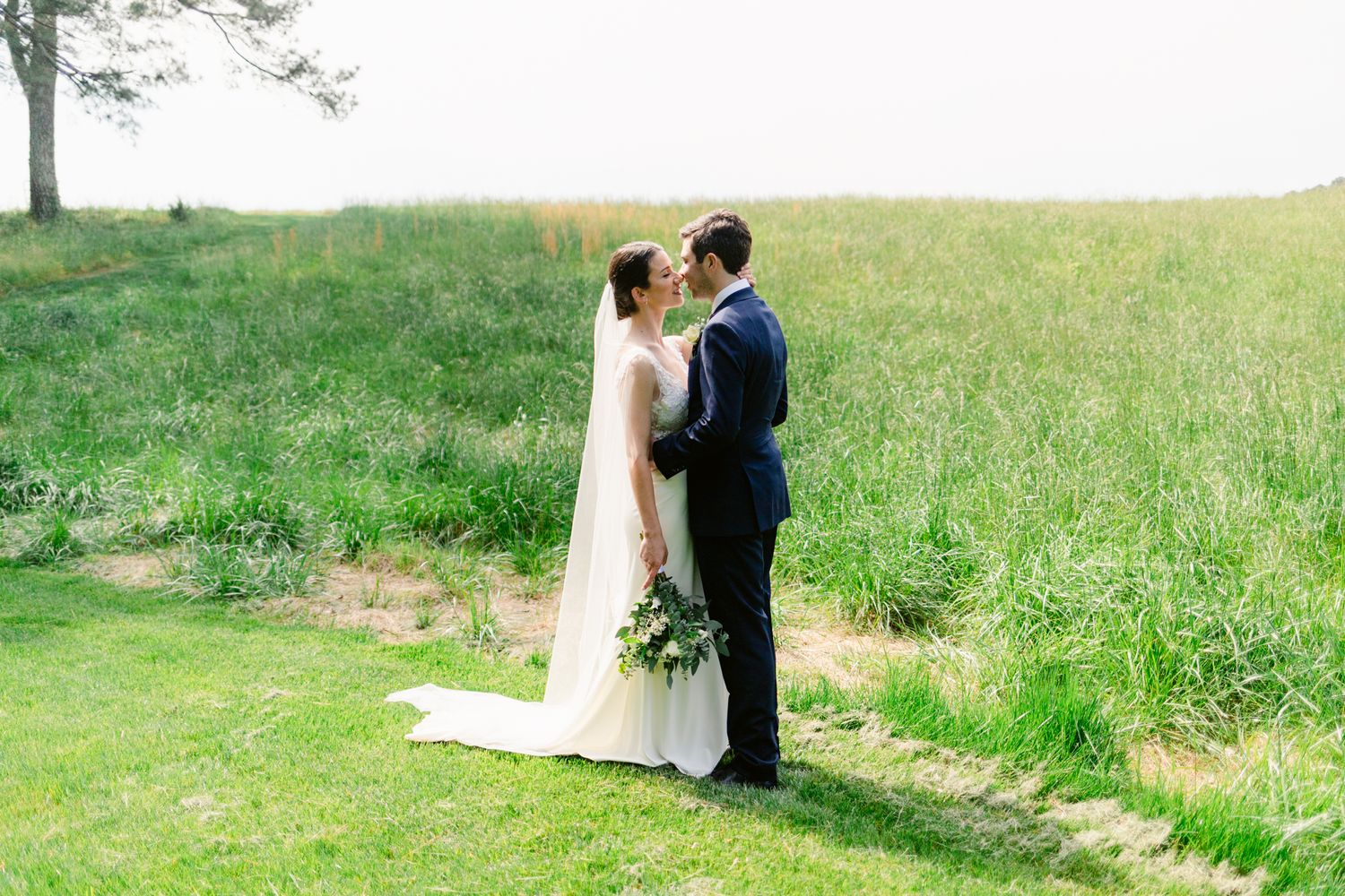 A couple shares an intimate moment in a sunlit meadow during their wedding photoshoot.