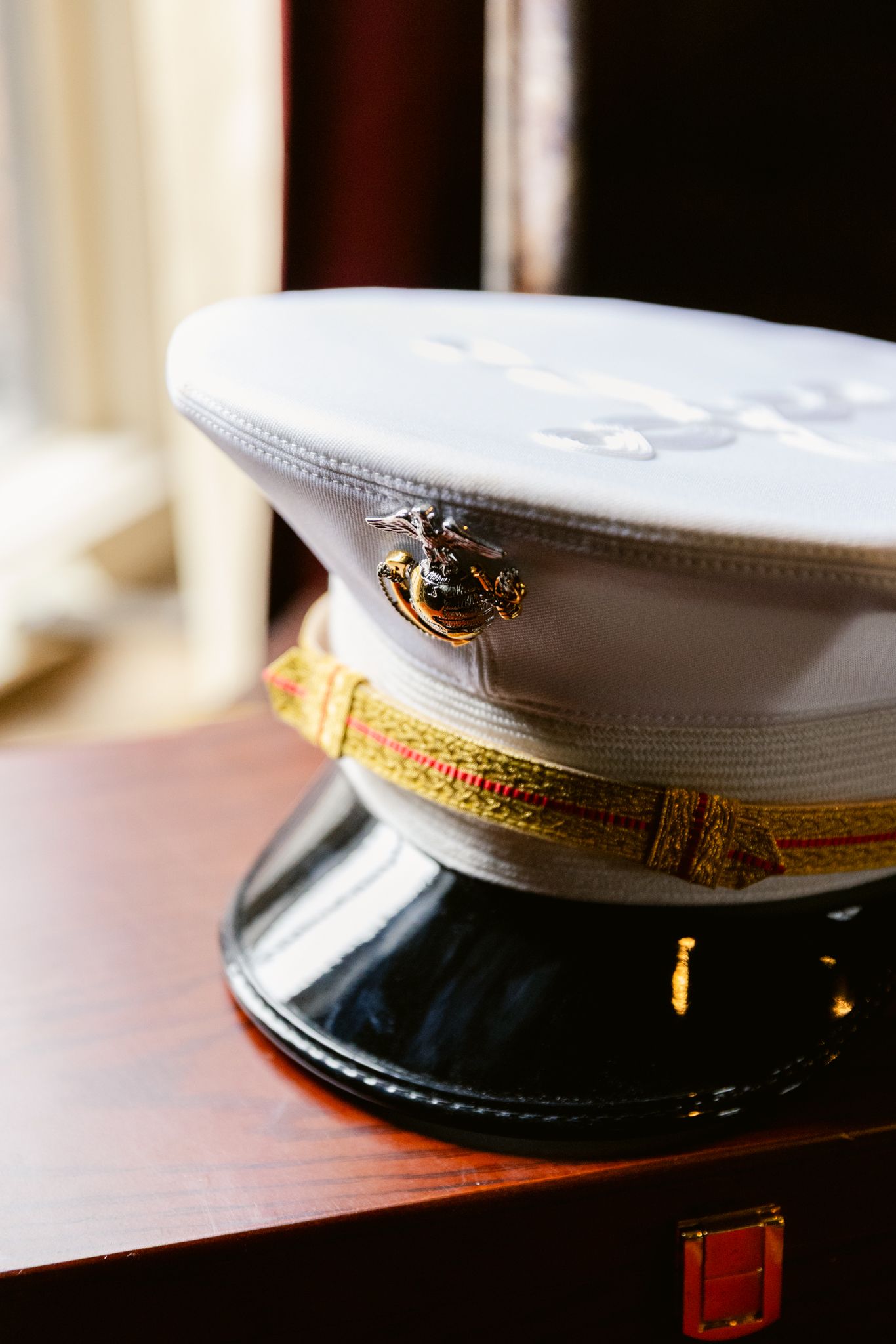 A white U.S. Marine Corps dress uniform cap with gold trim and eagle emblem sits on a wooden surface.