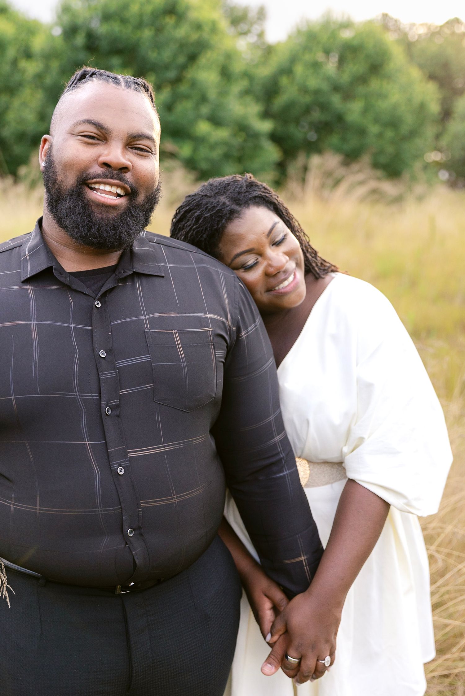 Happy couple sharing joyful candid moments together in a sunlit outdoor field setting.