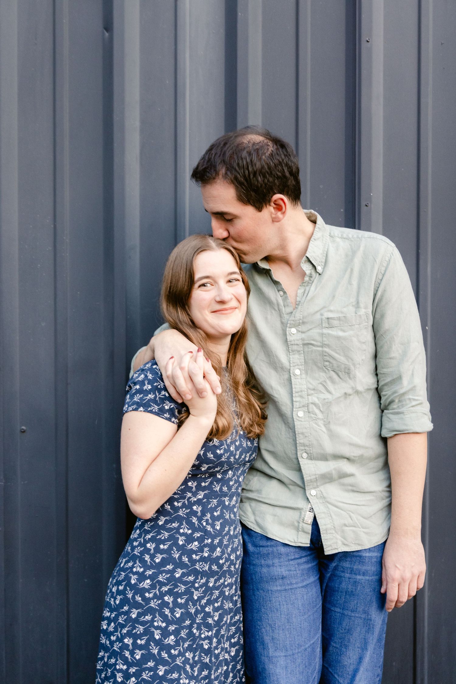 A couple shares intimate moments and laughter against a gray corrugated metal wall in a series of candid photos.