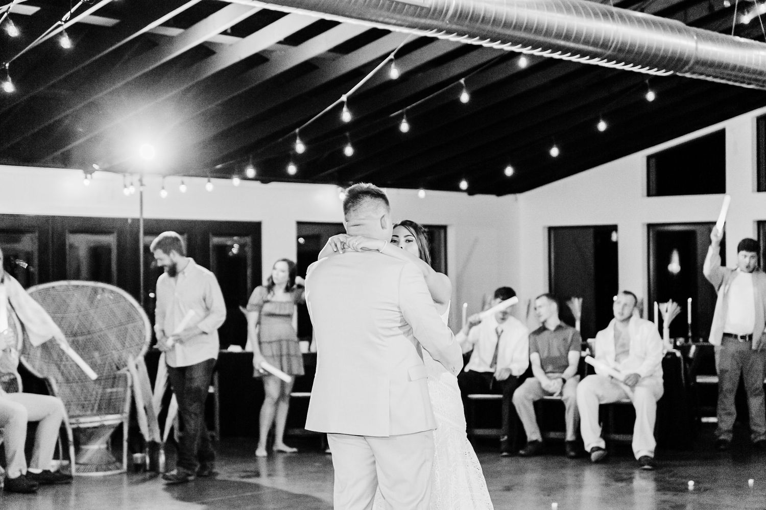 Wedding guests dance in a line during a reception under twinkling string lights in a dark venue.
